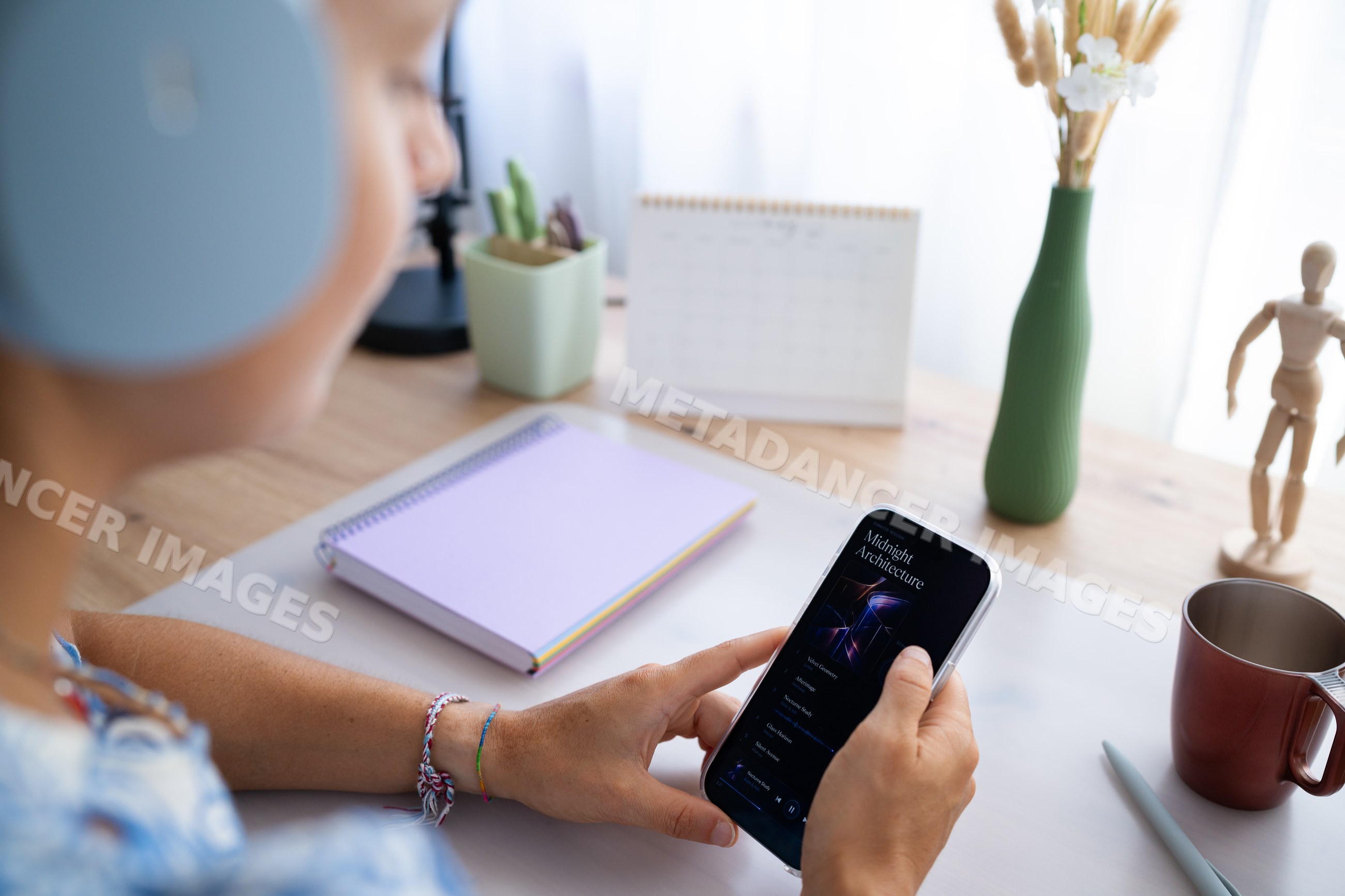 White person holding smartphone listening to music at home office desk