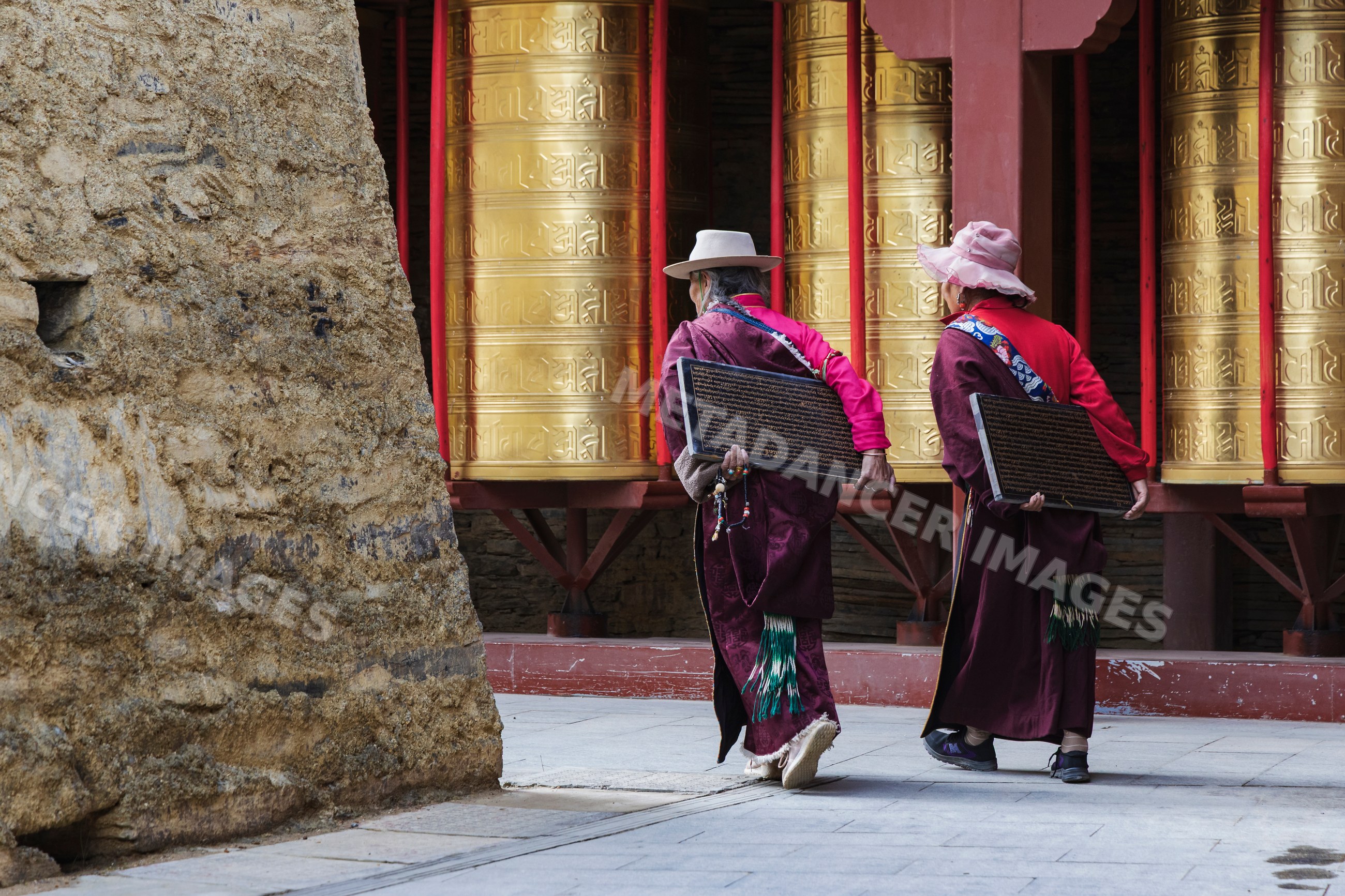 Tibetan women carrying inscribed tablets at Mani Wall prayer wheels