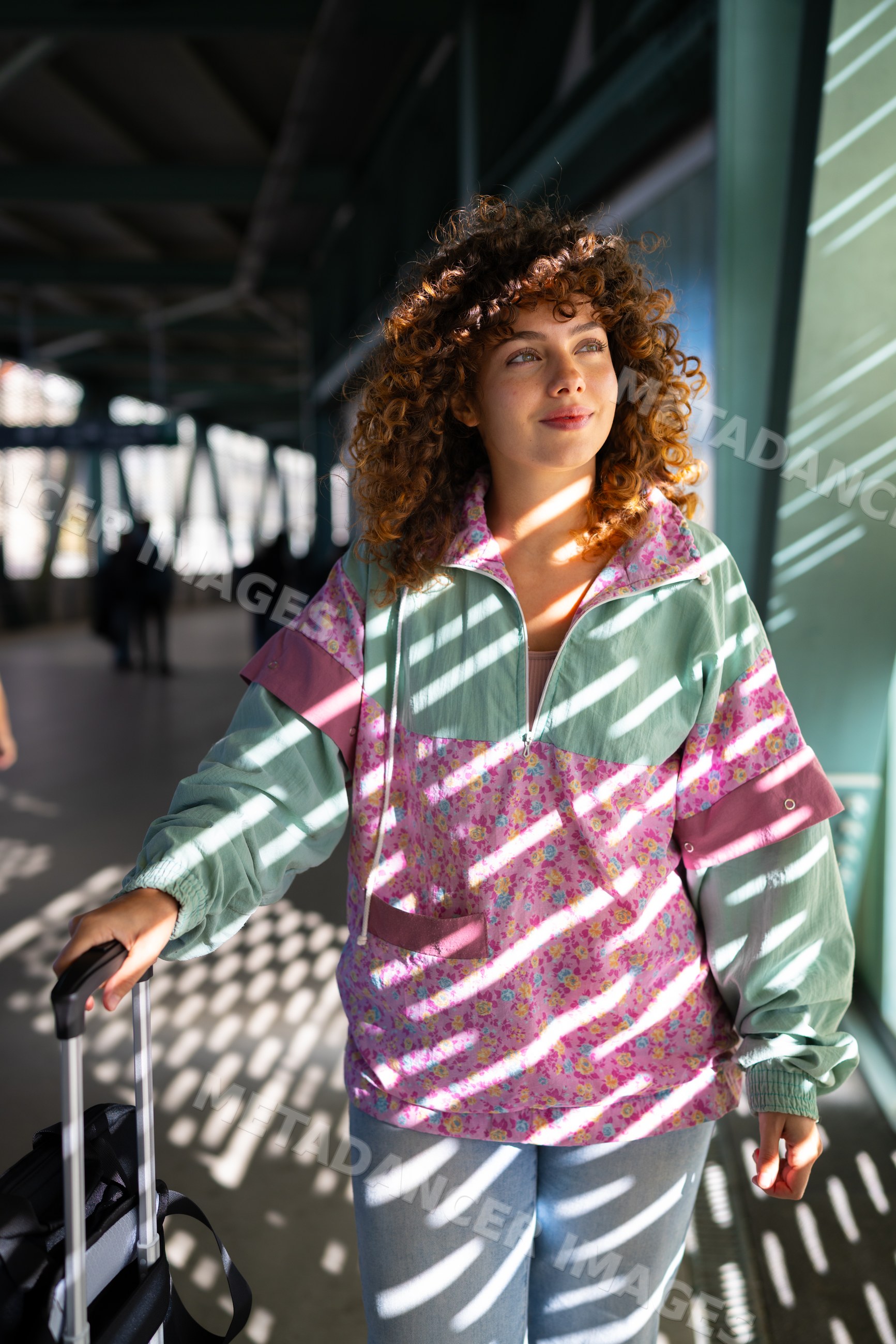 White woman walking and pulling suitcase in sunlit corridor in Spain