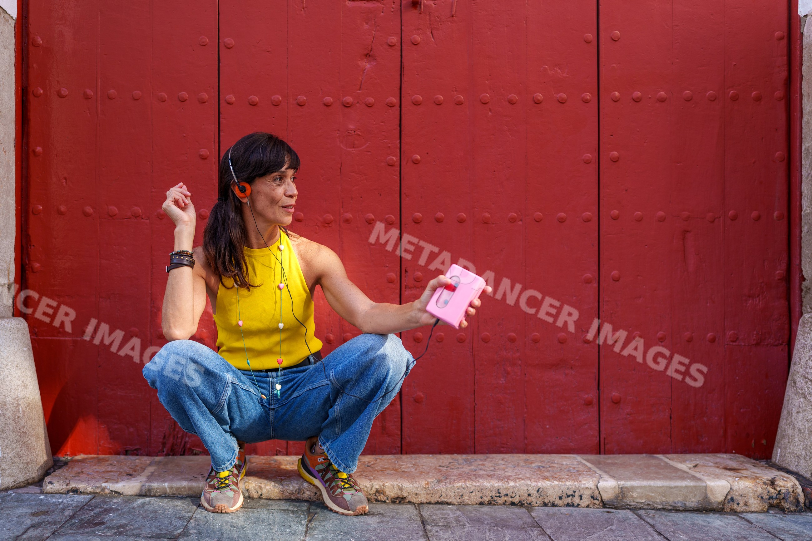 Hispanic woman listening to music on cassette player squatting by red
