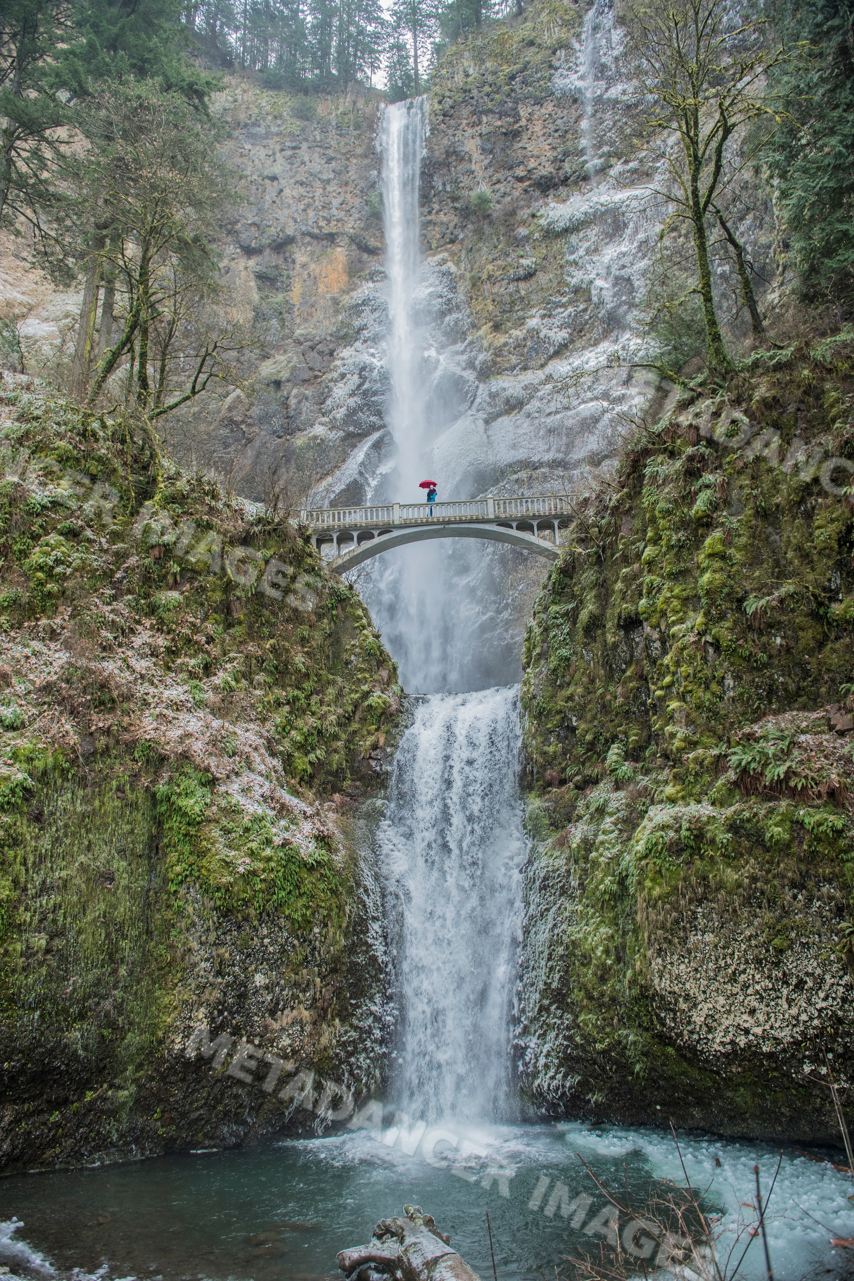 Waterfall with bridge and white person holding umbrella
