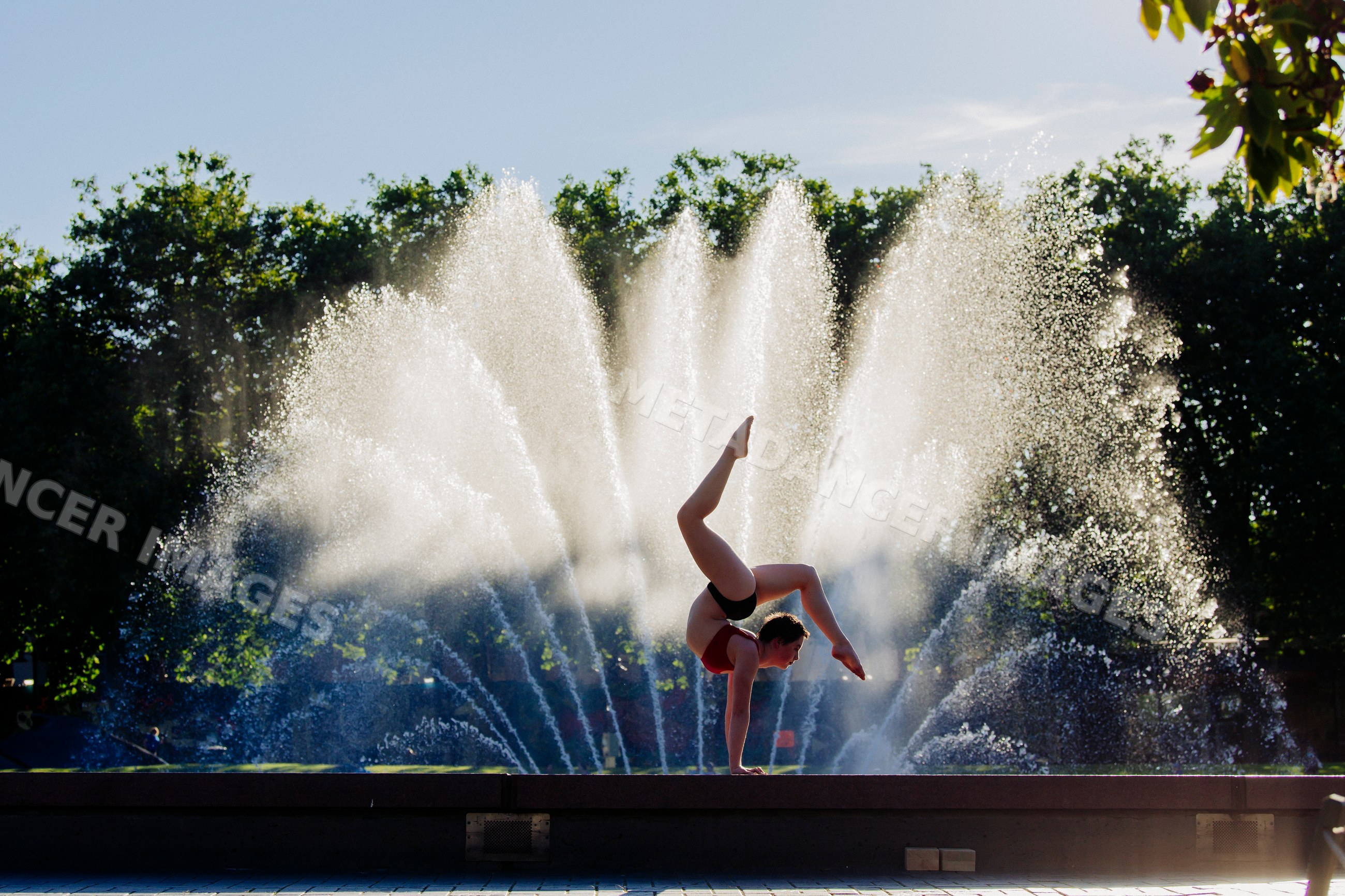 Handstand acrobat balancing in front of water fountain in outdoor park