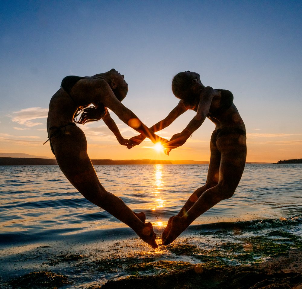 Two women practicing partner yoga acrobatics at beach sunset in wa USA