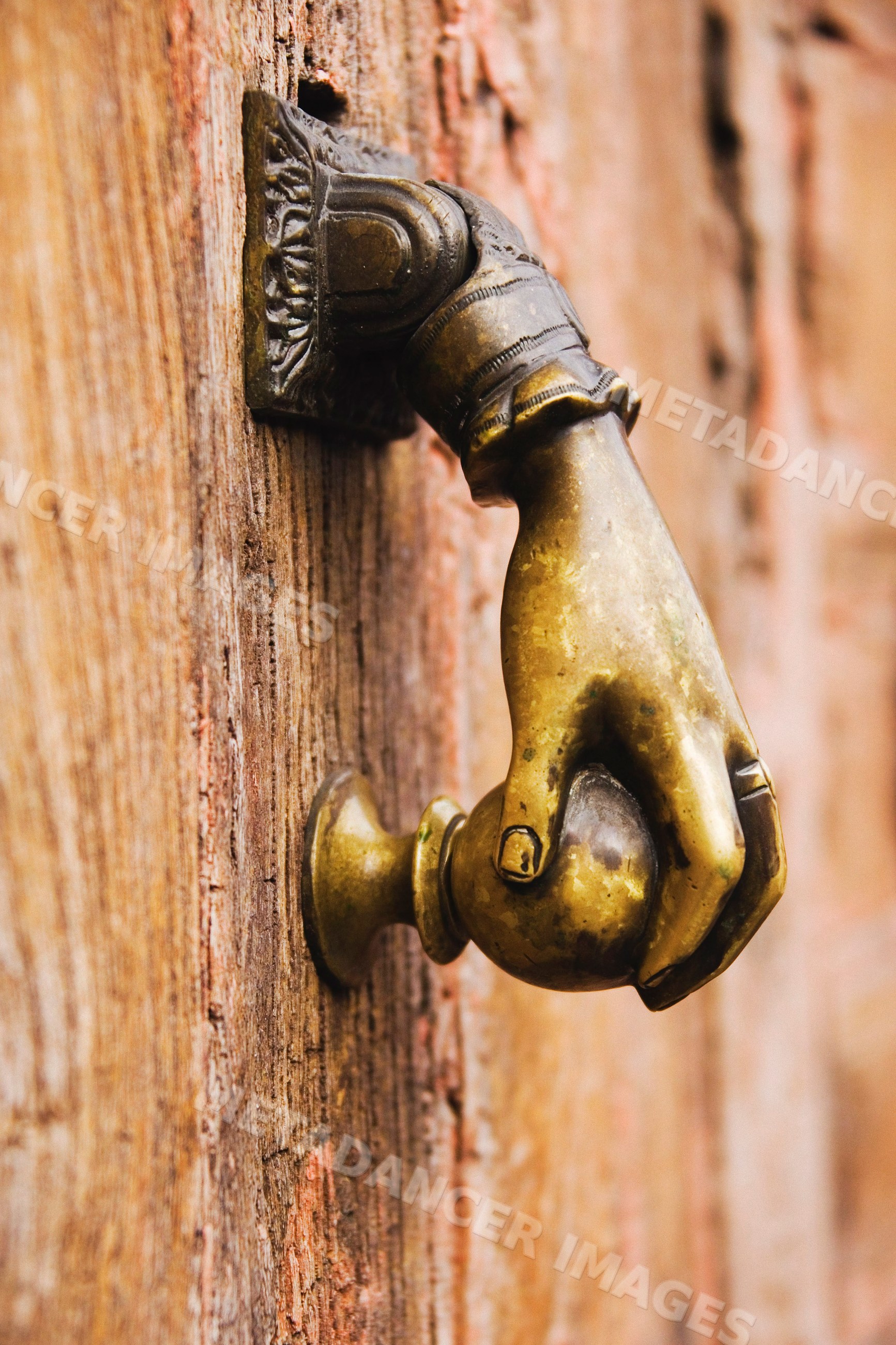 Close-up of bronze hand-shaped door knocker on wooden door