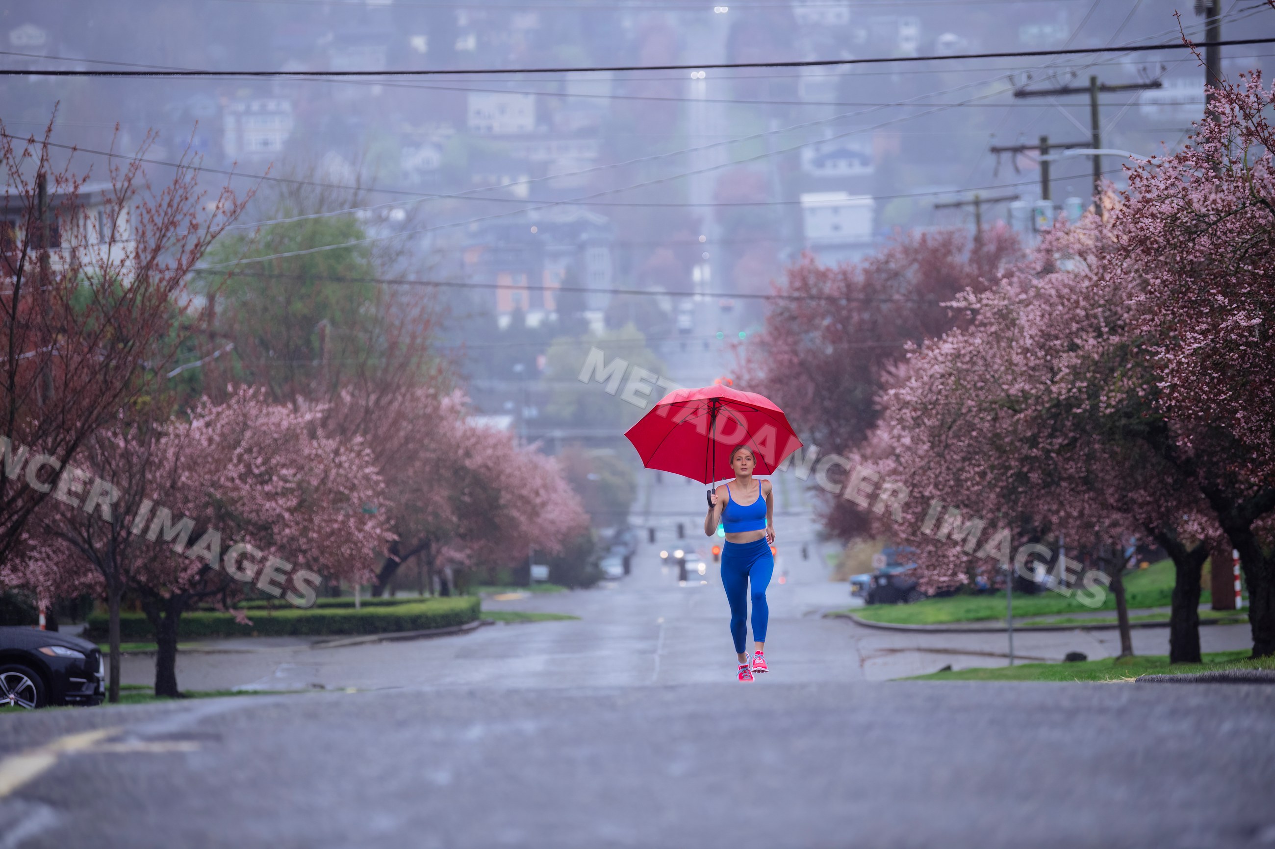 White woman running on rainy urban street with umbrella and blossoming