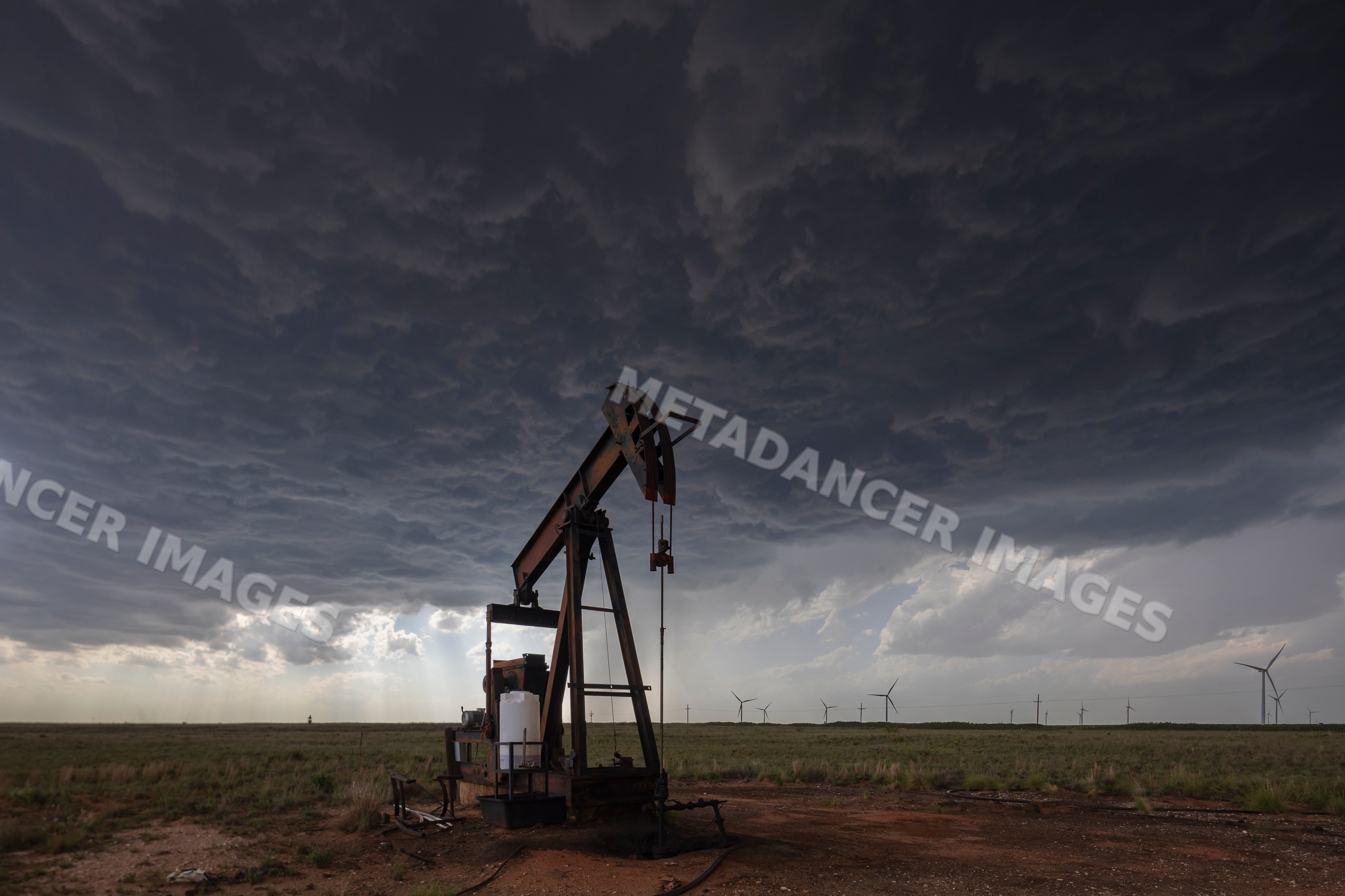 Pump jack under dark storm clouds with wind turbines on Great Plains