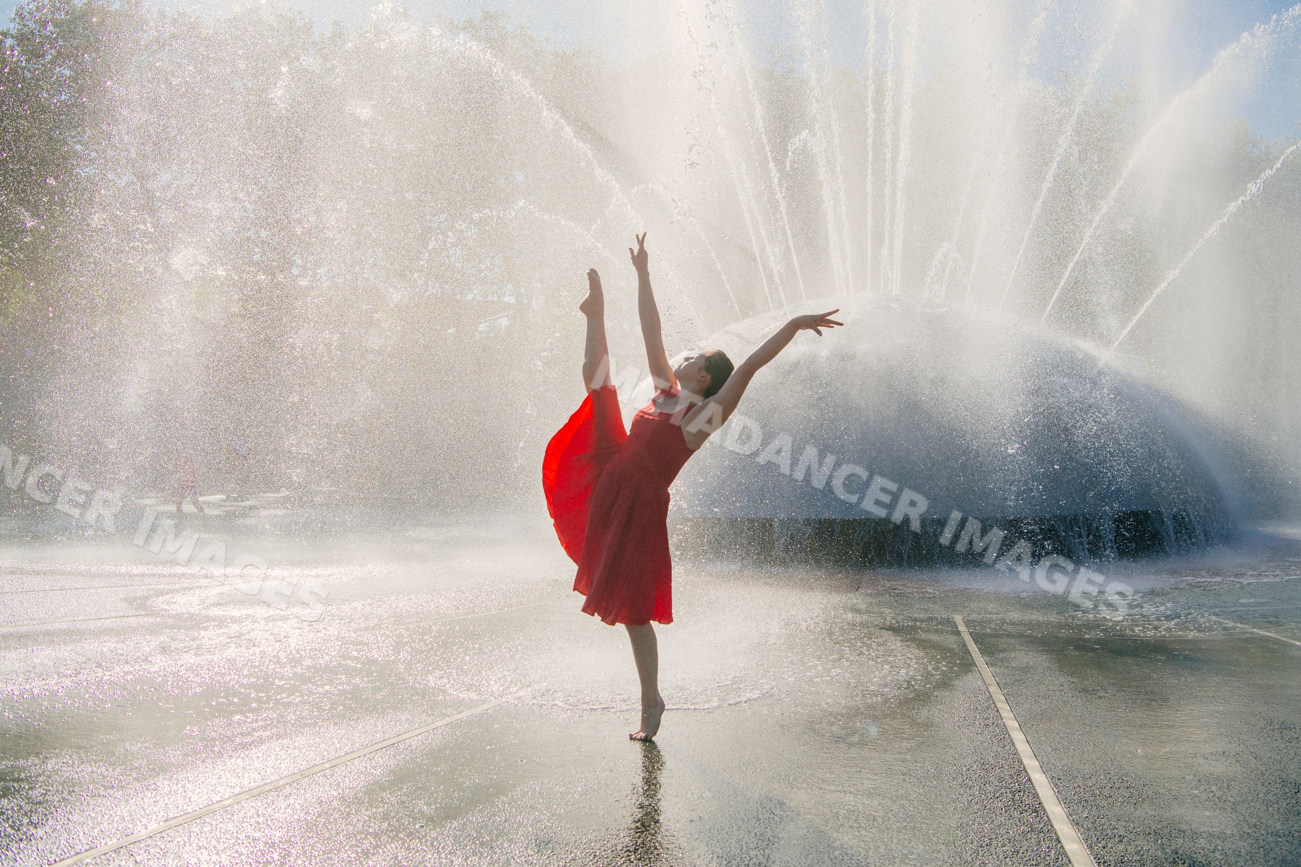 White dancer in red dress striking a graceful pose by outdoor water
