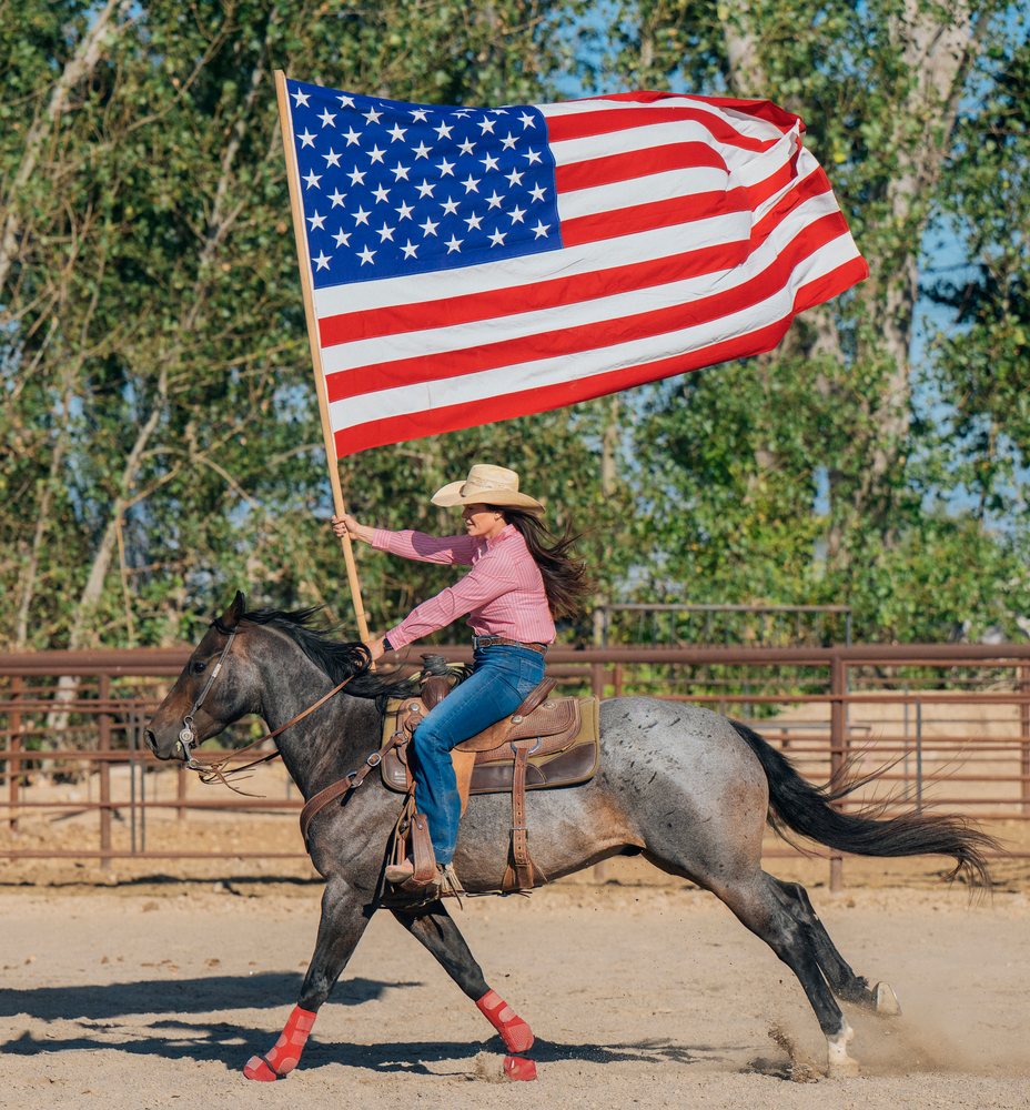 White woman riding horse carrying american flag