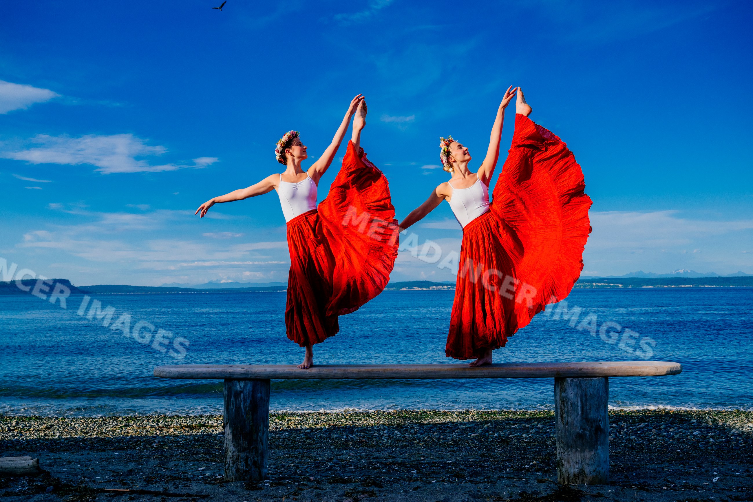 Two white women performing partner acrobatics yoga poses by the water