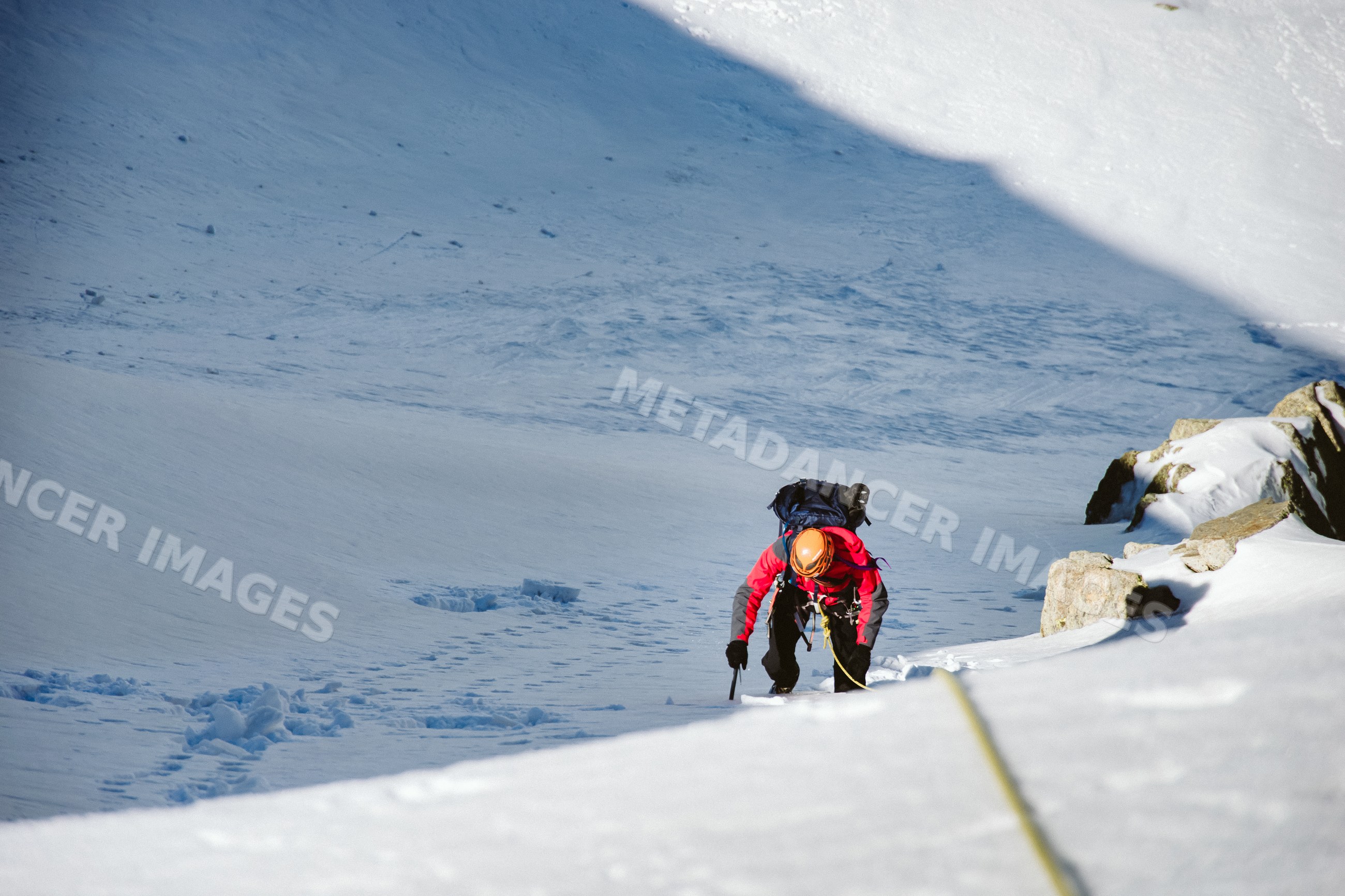 Mountaineer climbing snow slope with ice axe and rope