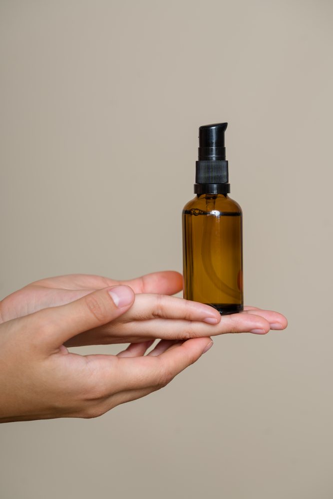 Hand holding amber glass pump dispenser bottle