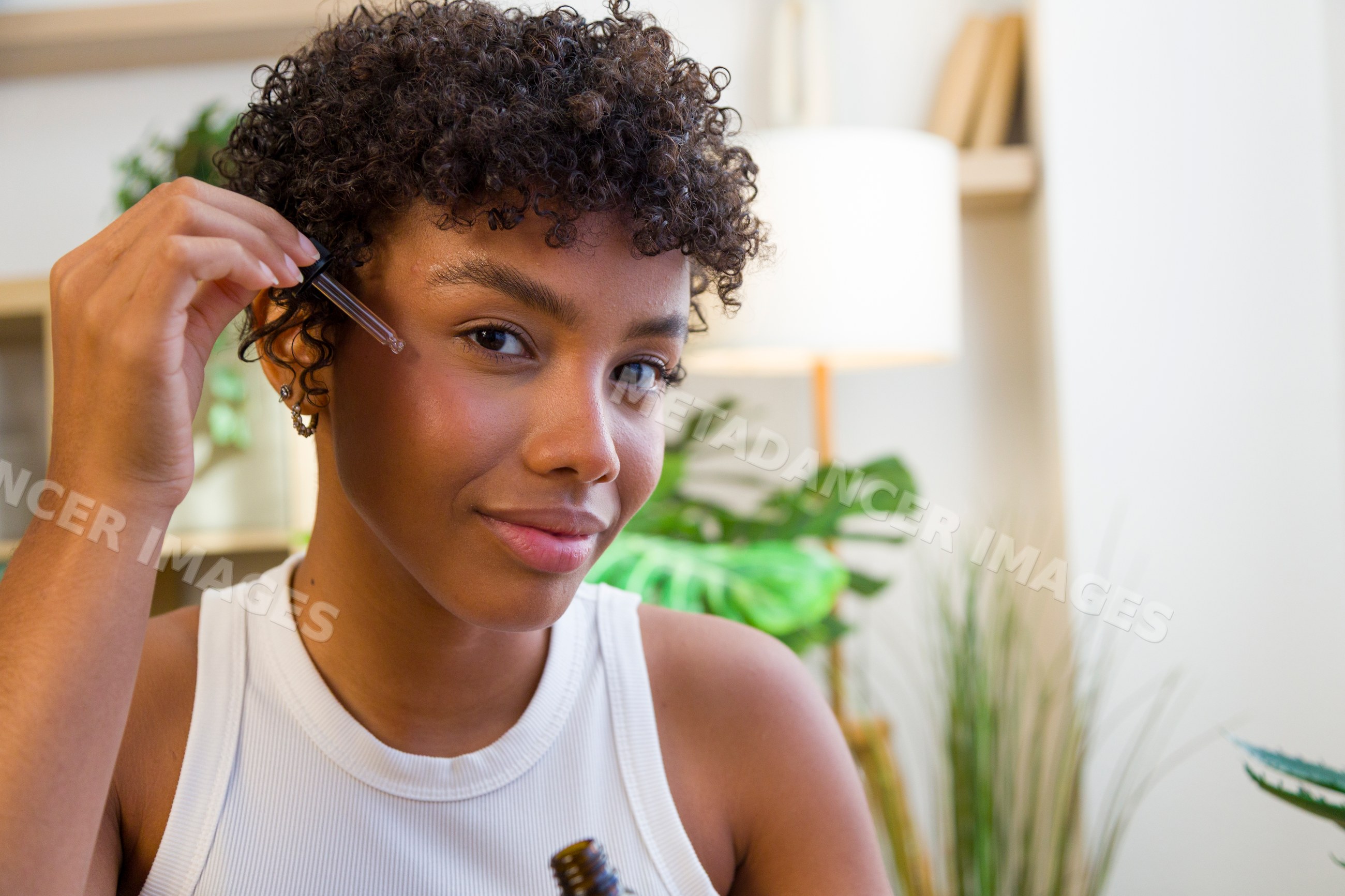 Young African American woman applying serum to face indoors at home