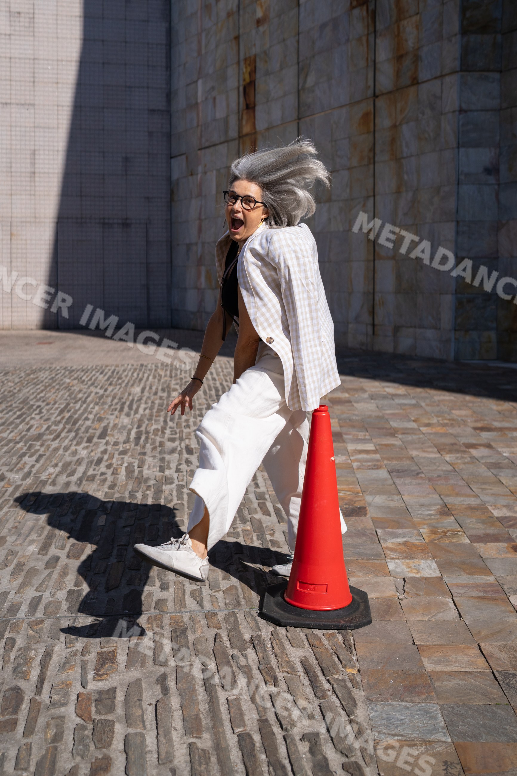 White woman walking near red traffic cone on paved plaza in sunlight