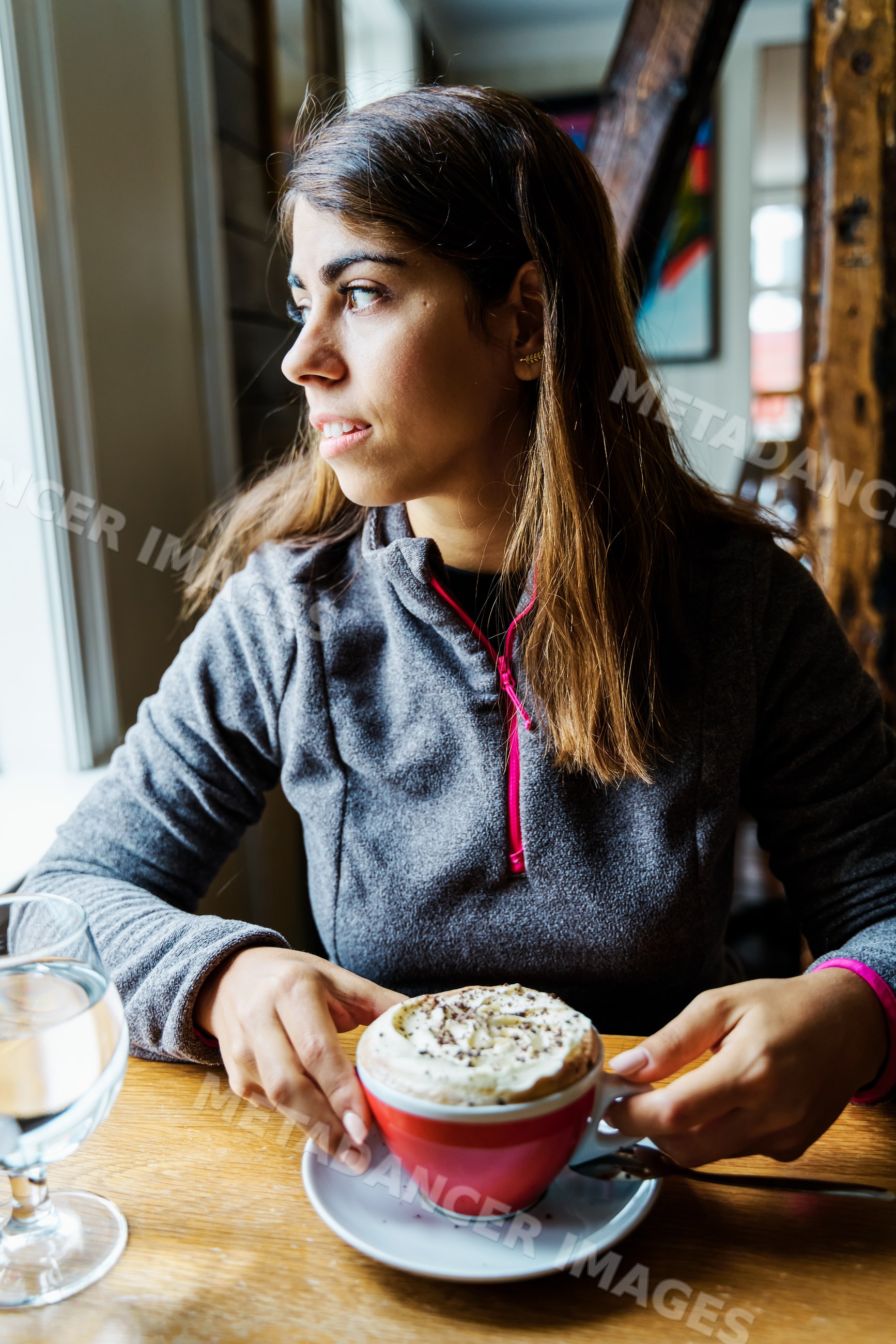 A white woman enjoys a cappuccino inside a cozy cafe