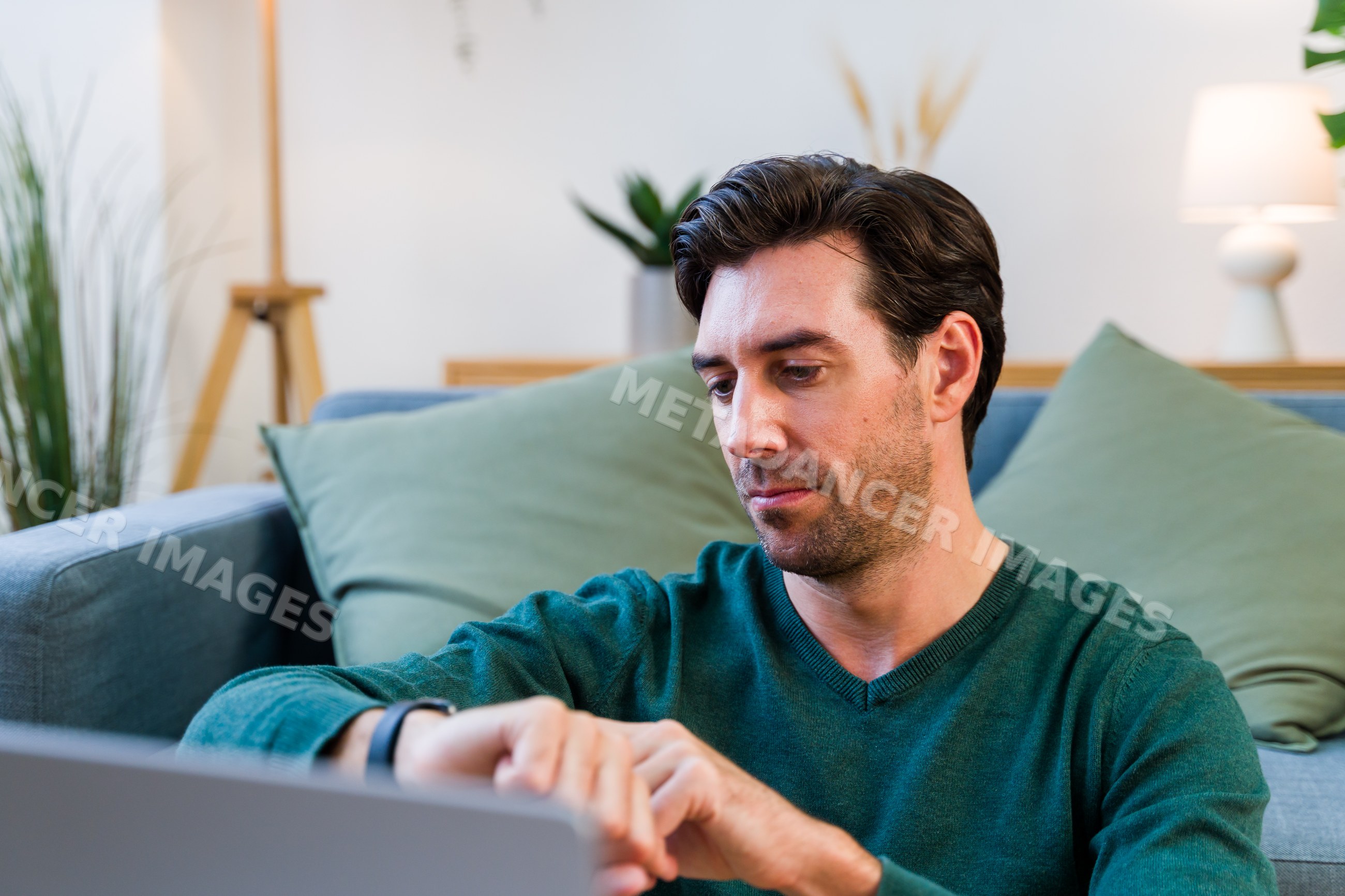 White man checking wristwatch while sitting on couch in living room