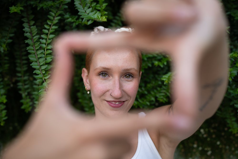 A white woman smiles framing her face with hands outdoors