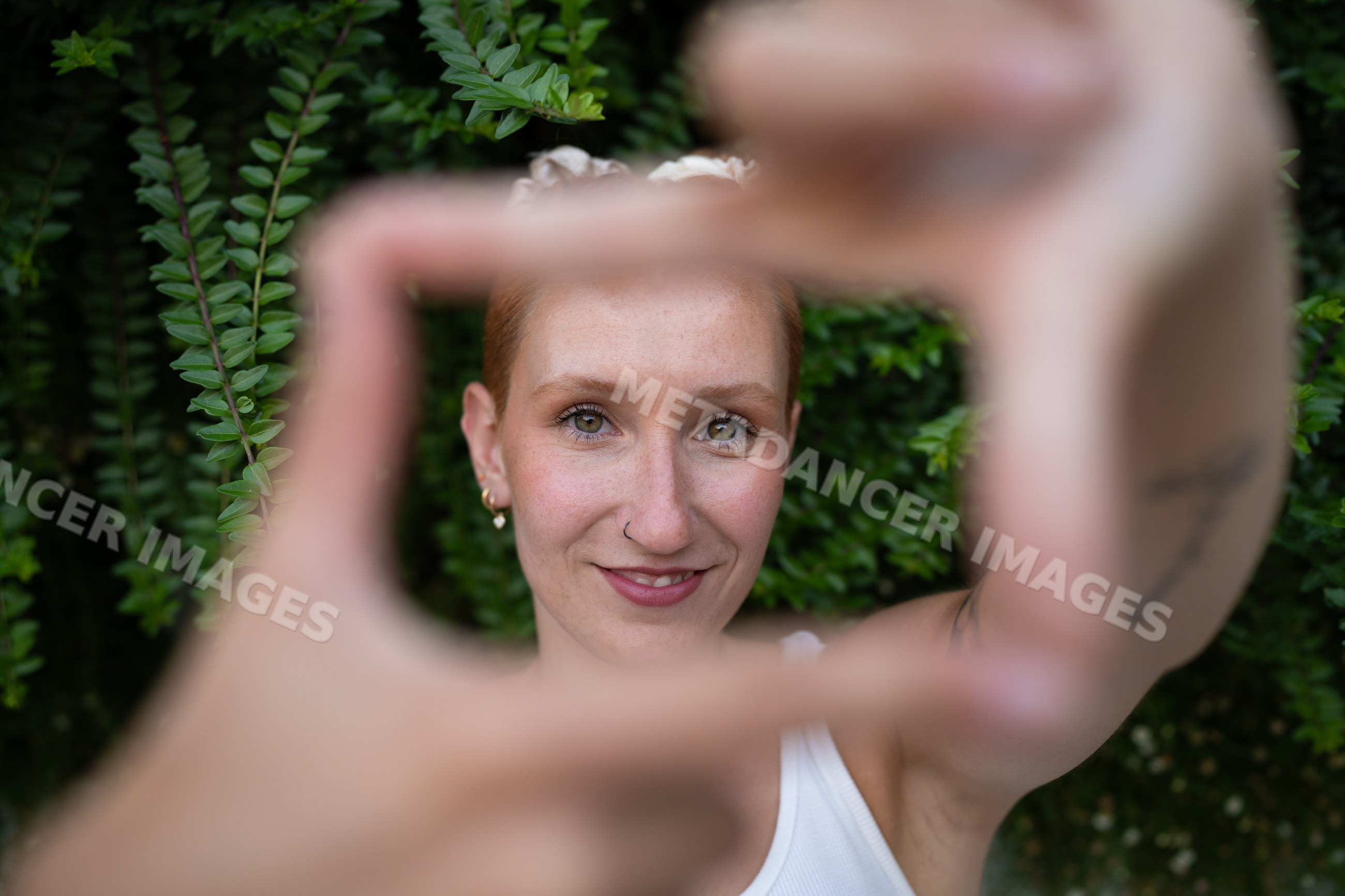 A white woman smiles framing her face with hands outdoors
