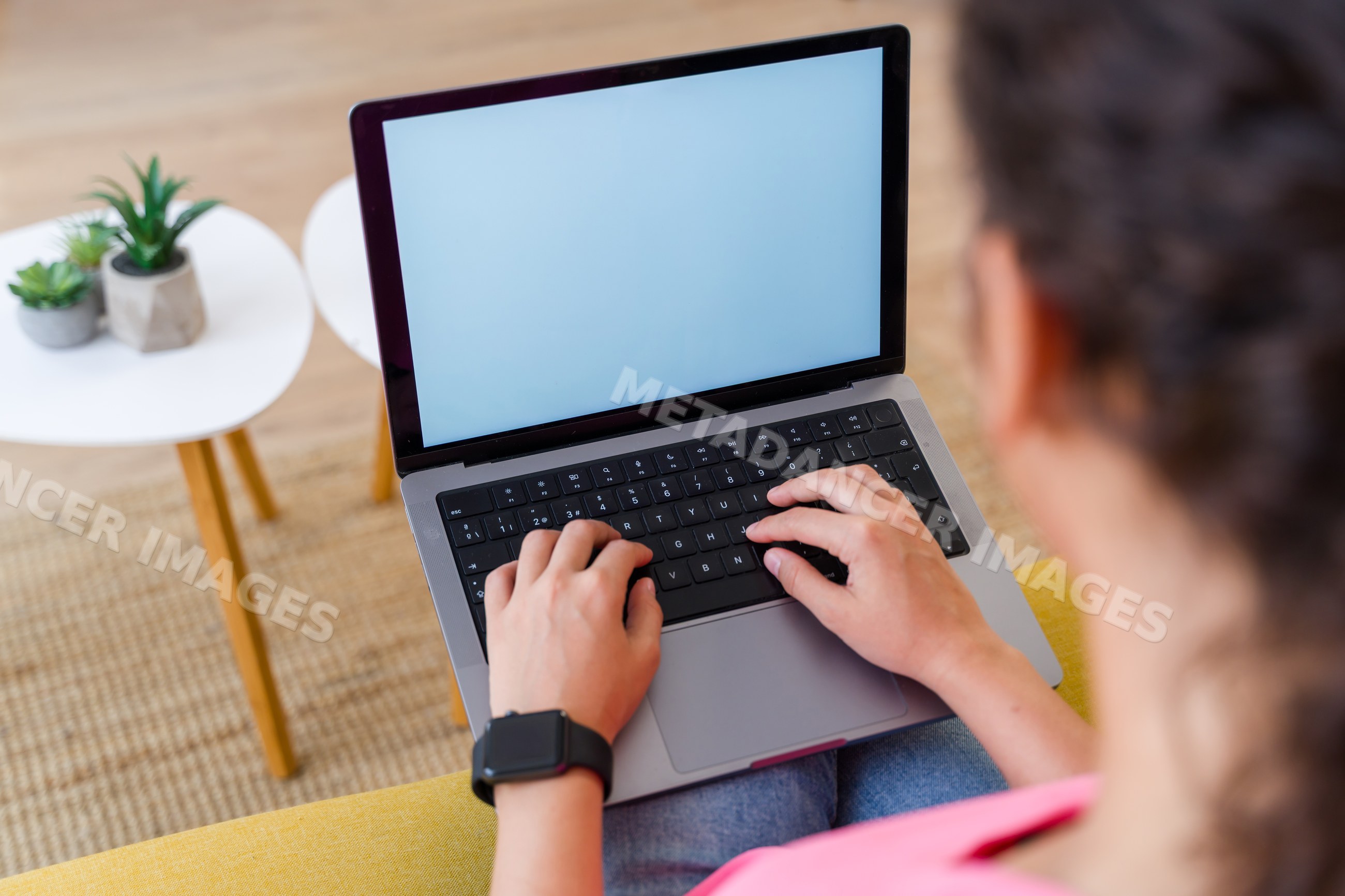 Hispanic Person typing on a laptop indoors with plants on a small