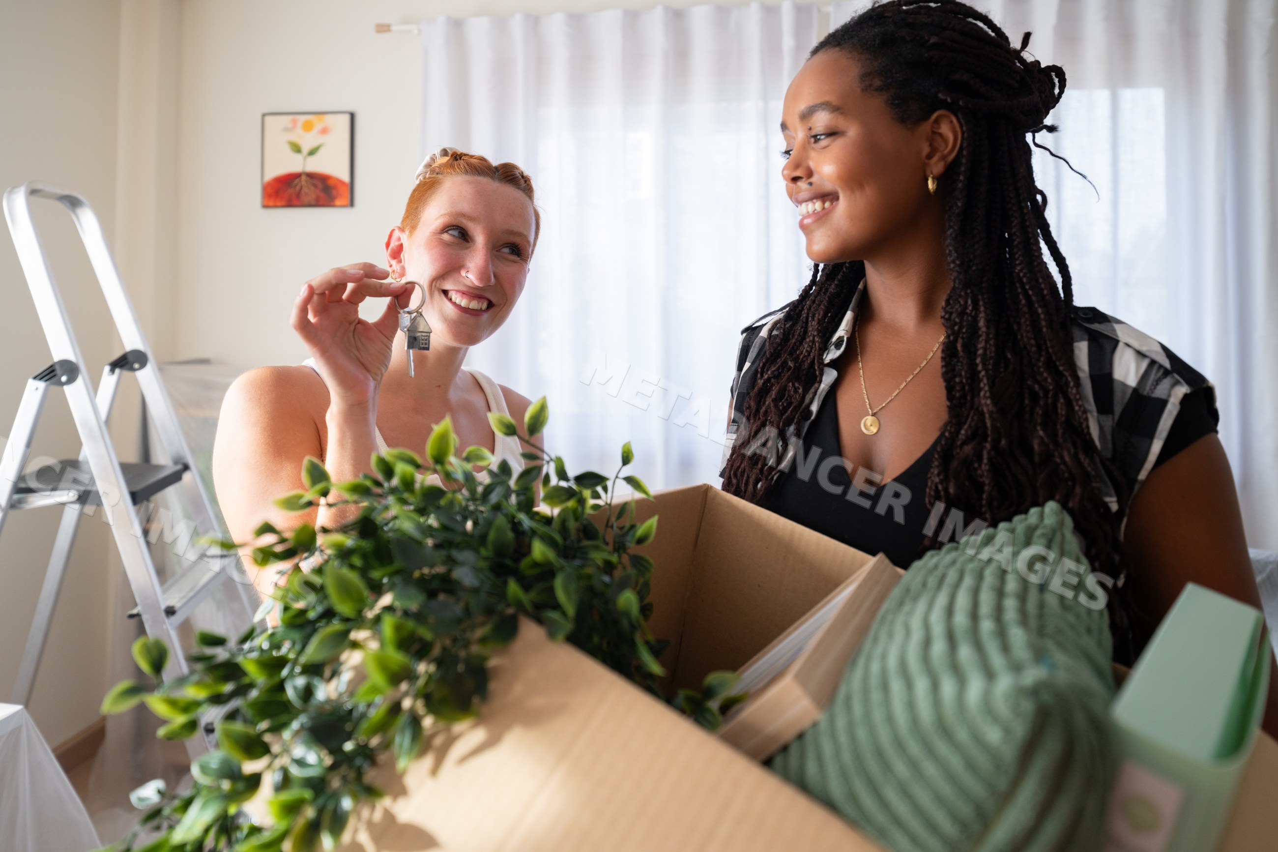 Two African American women happily unpack moving boxes and hold keys