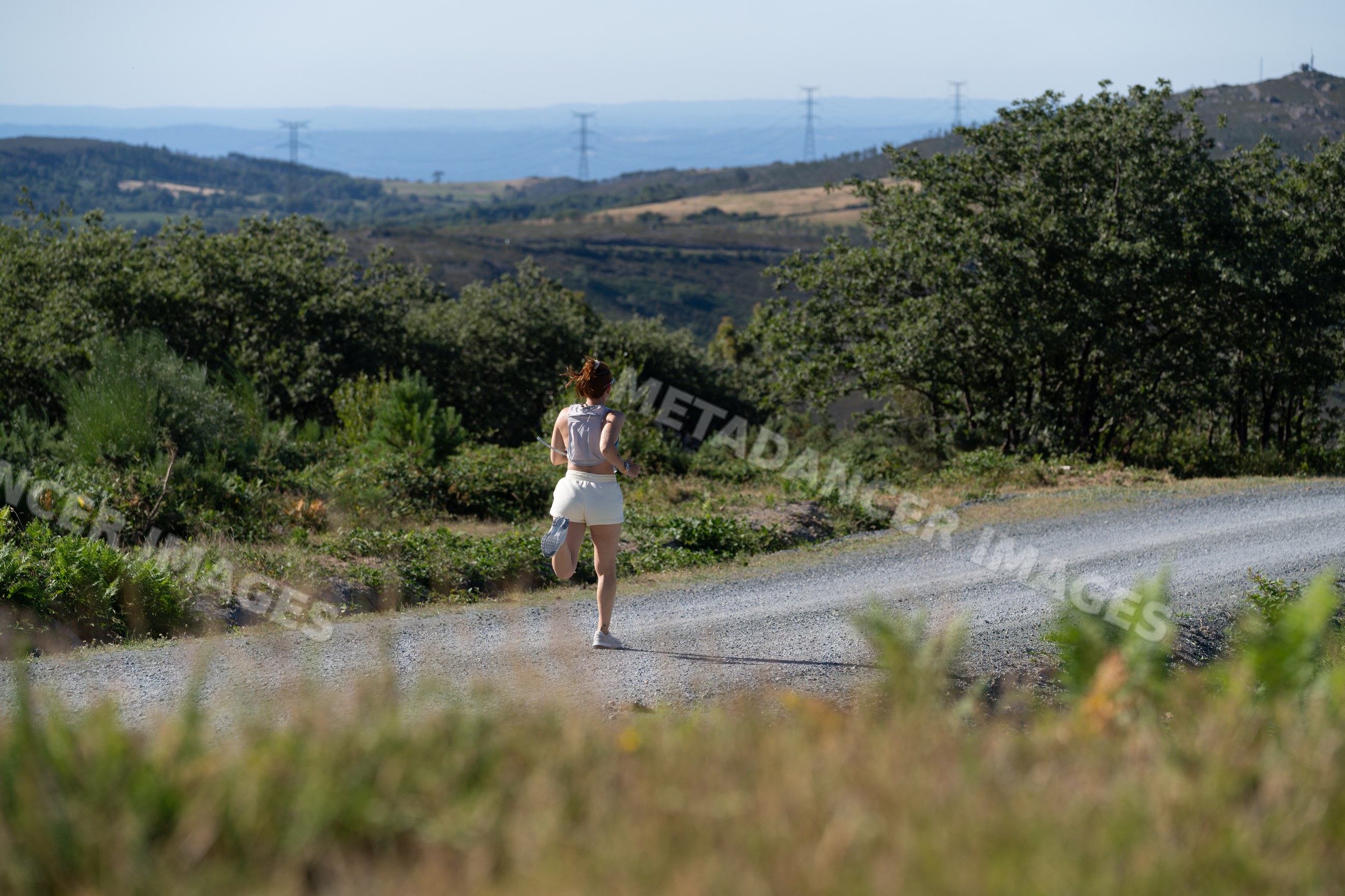 A white woman runs on a gravel trail surrounded by nature in Galicia