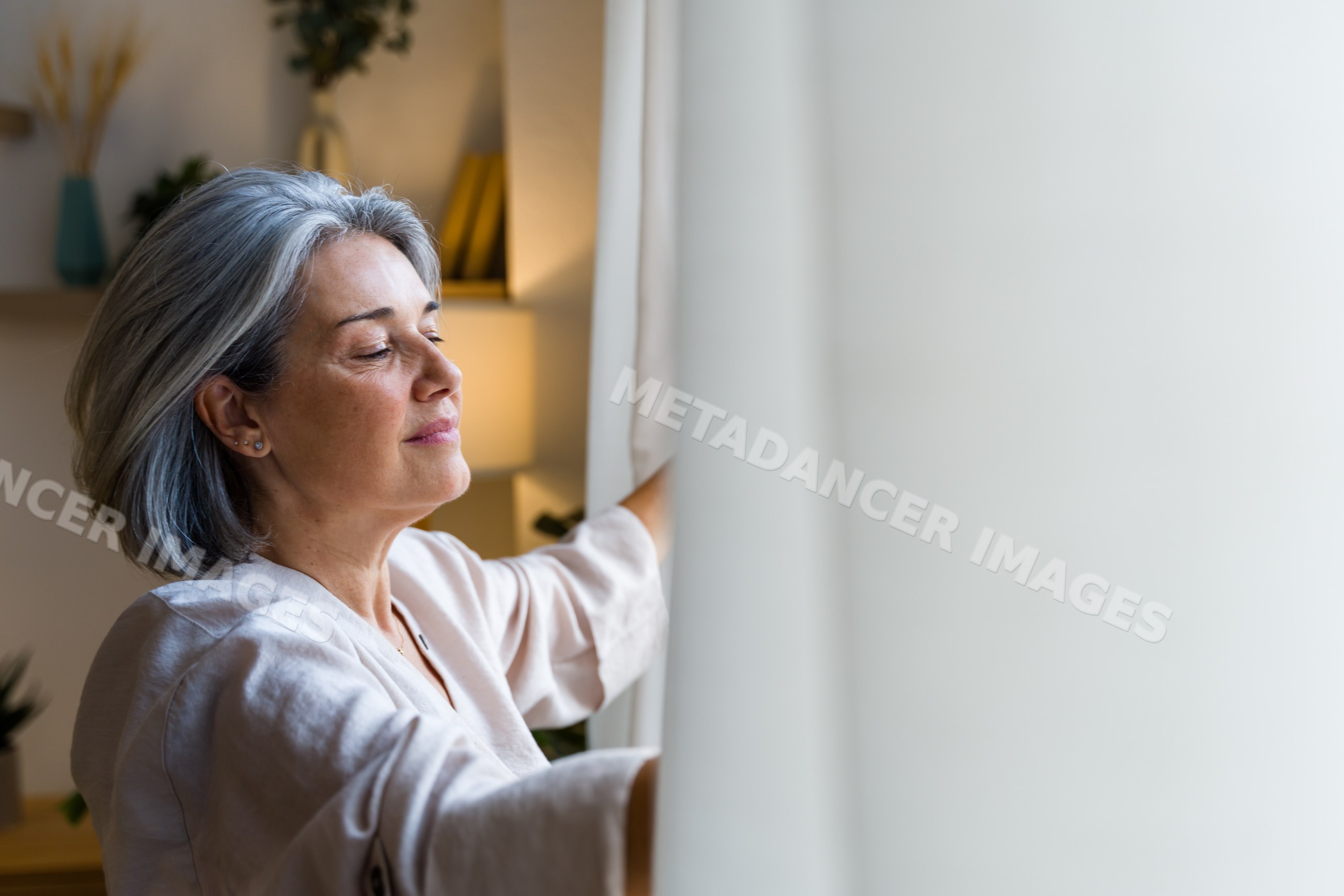 White woman opening curtains and enjoying a peaceful moment indoors