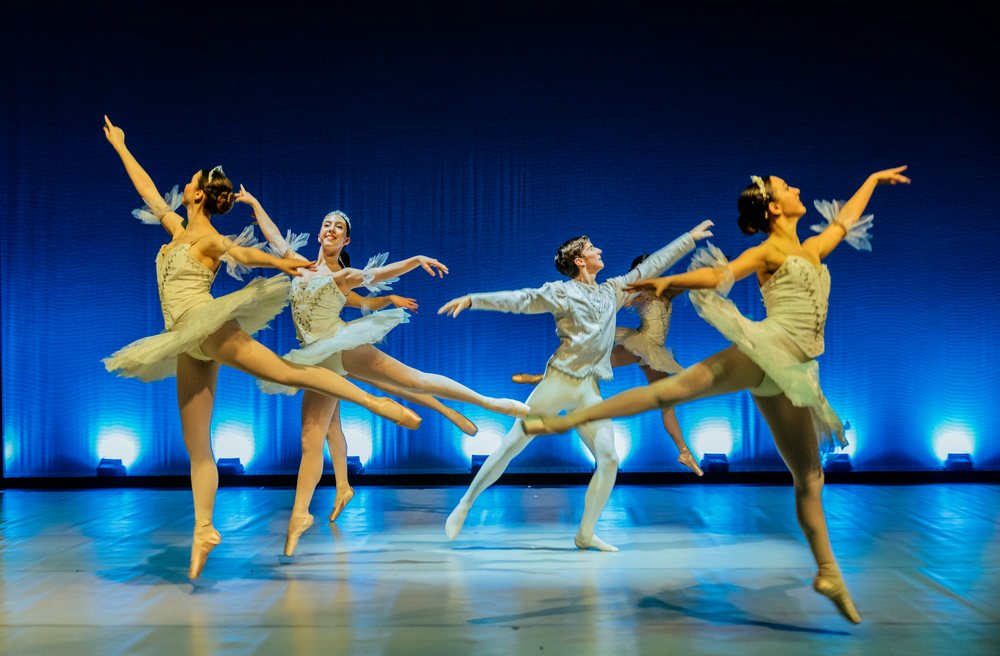 Ballet dancers perform a leap on stage in a holiday-themed ballet