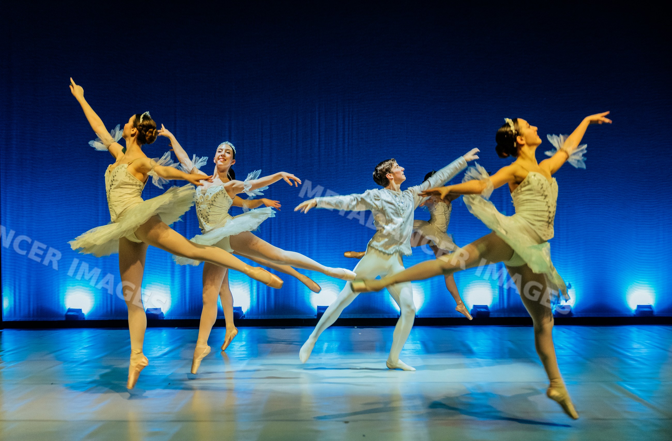 Ballet dancers perform a leap on stage in a holiday-themed ballet