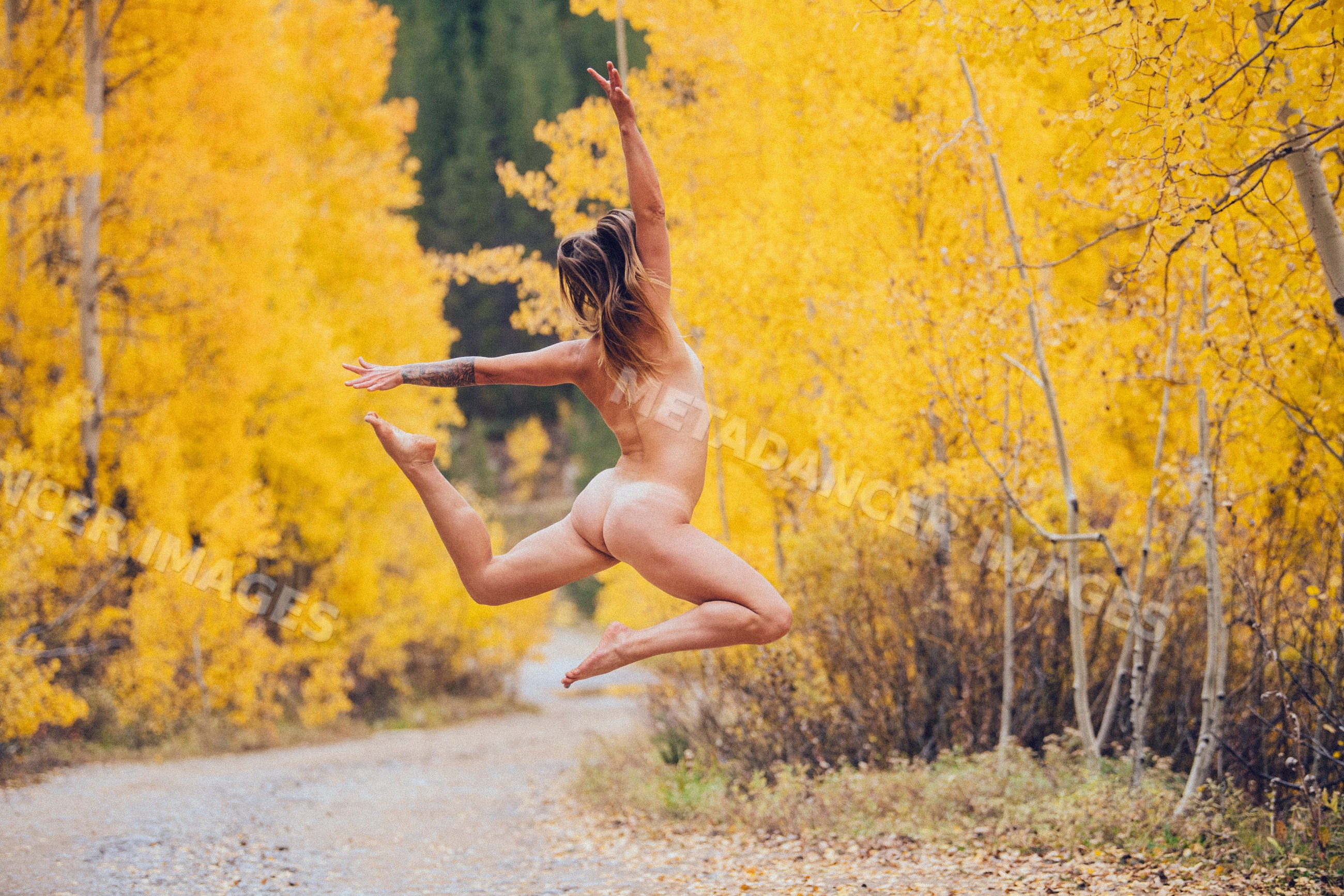 Nude white woman jumping on autumn forest trail in Durango Colorado