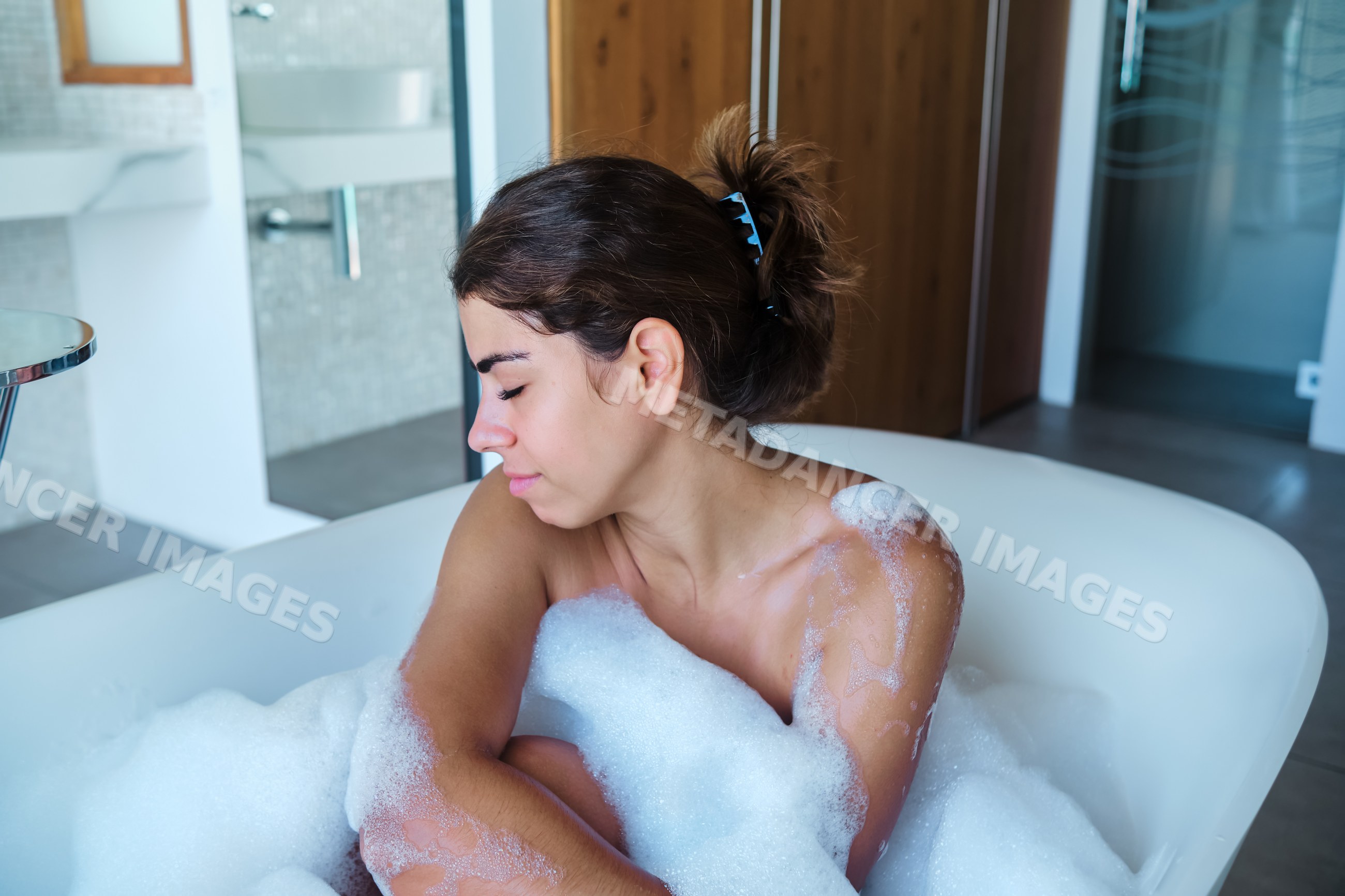 A white woman relaxing in a bubble bath in a modern bathroom