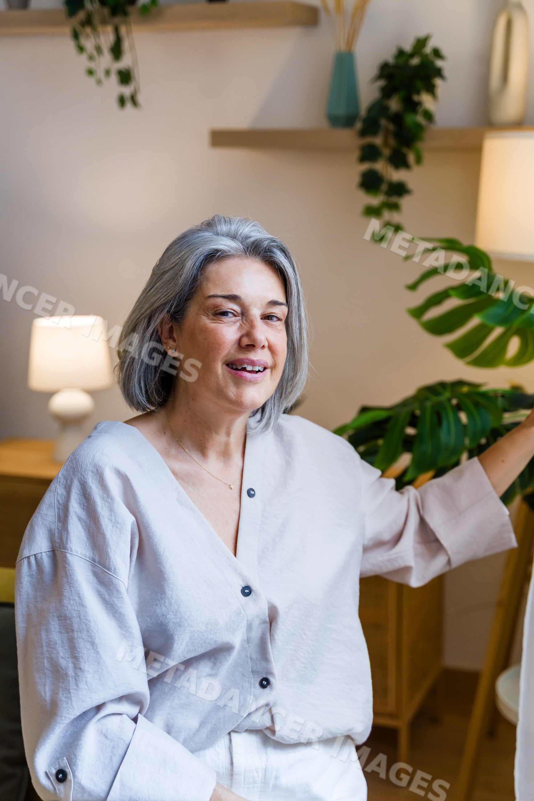 White woman smiling indoors near monstera plant in cozy living room