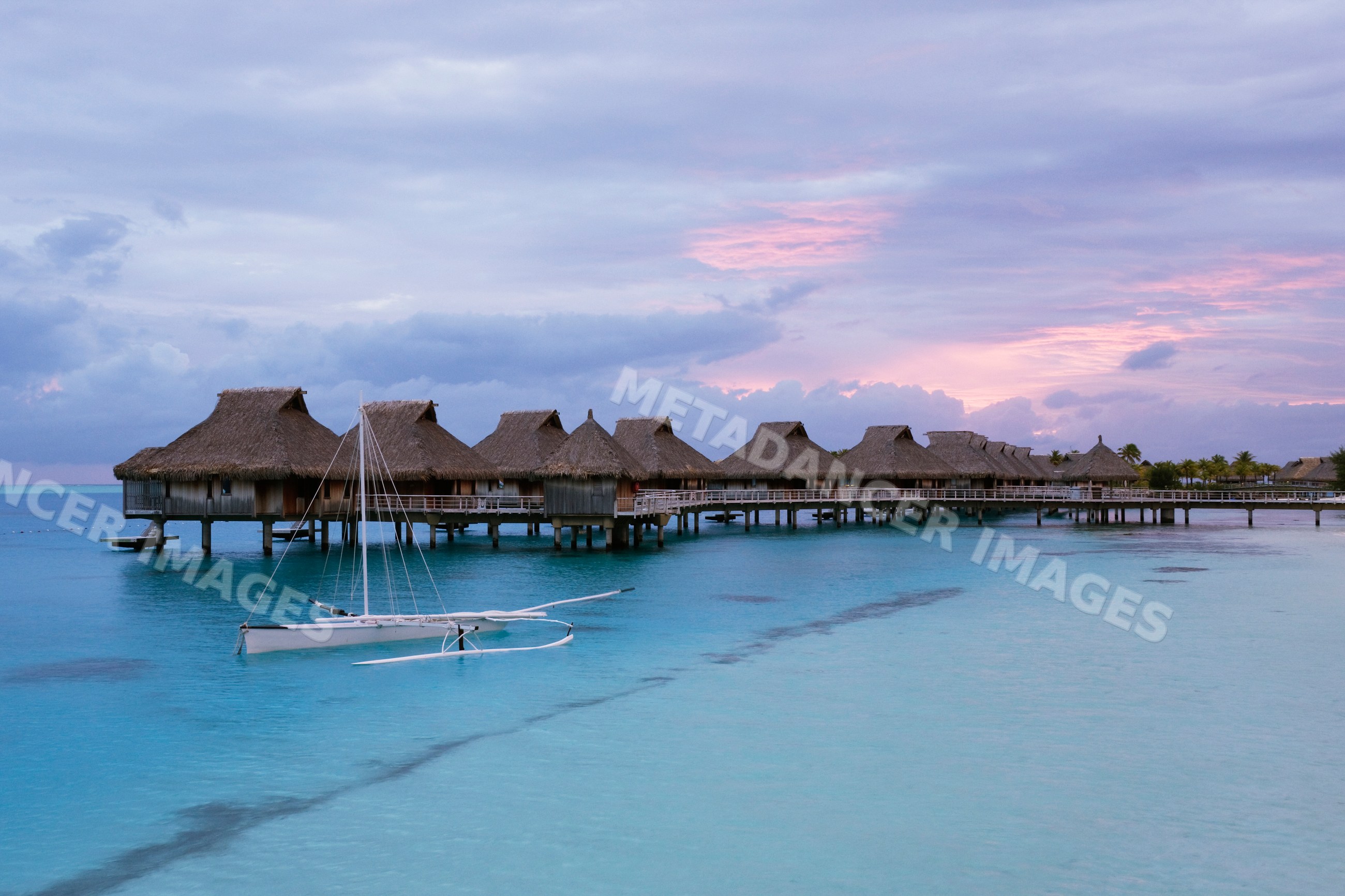 Overwater bungalows and a sailboat at bora nui resort during sunset