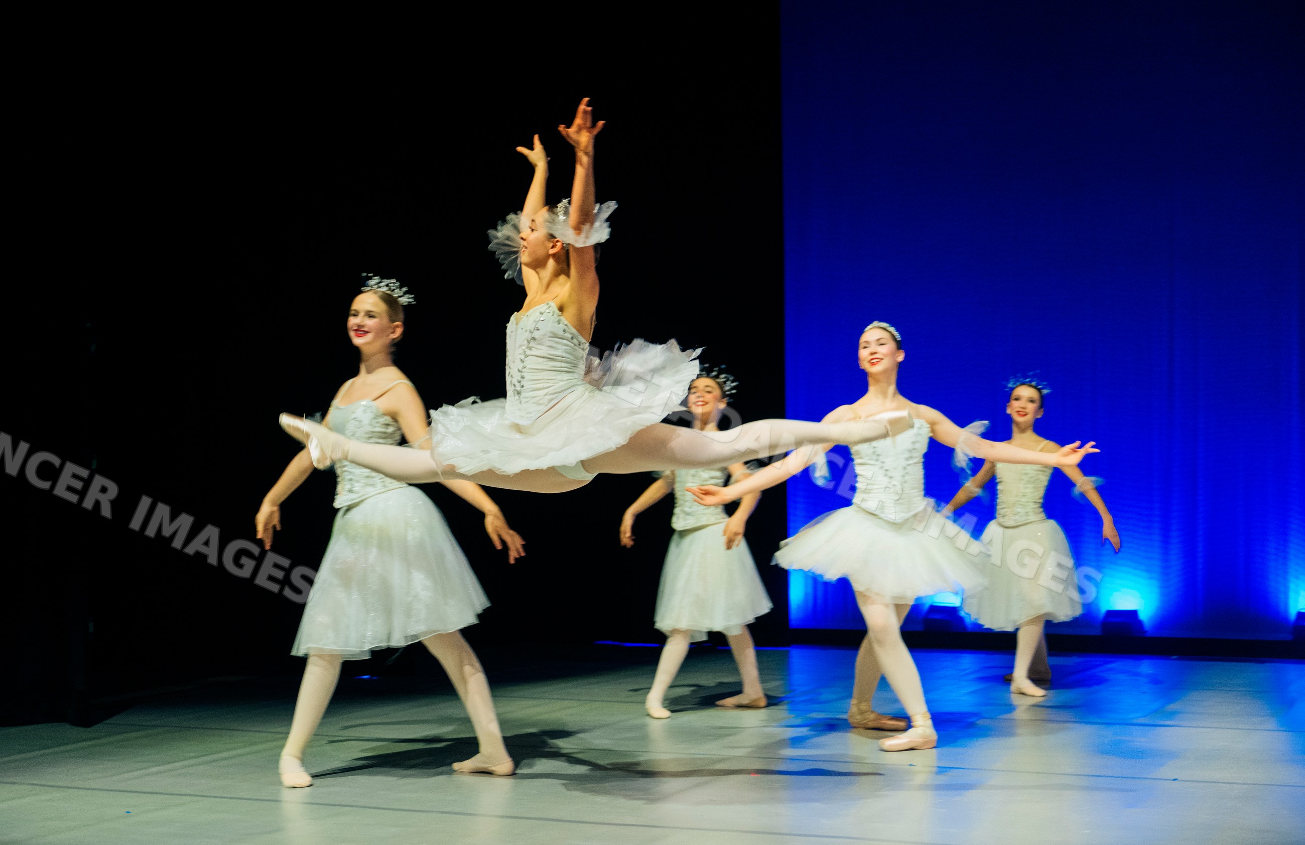 Ballet dancer performing a grand jeté leap on stage during recital