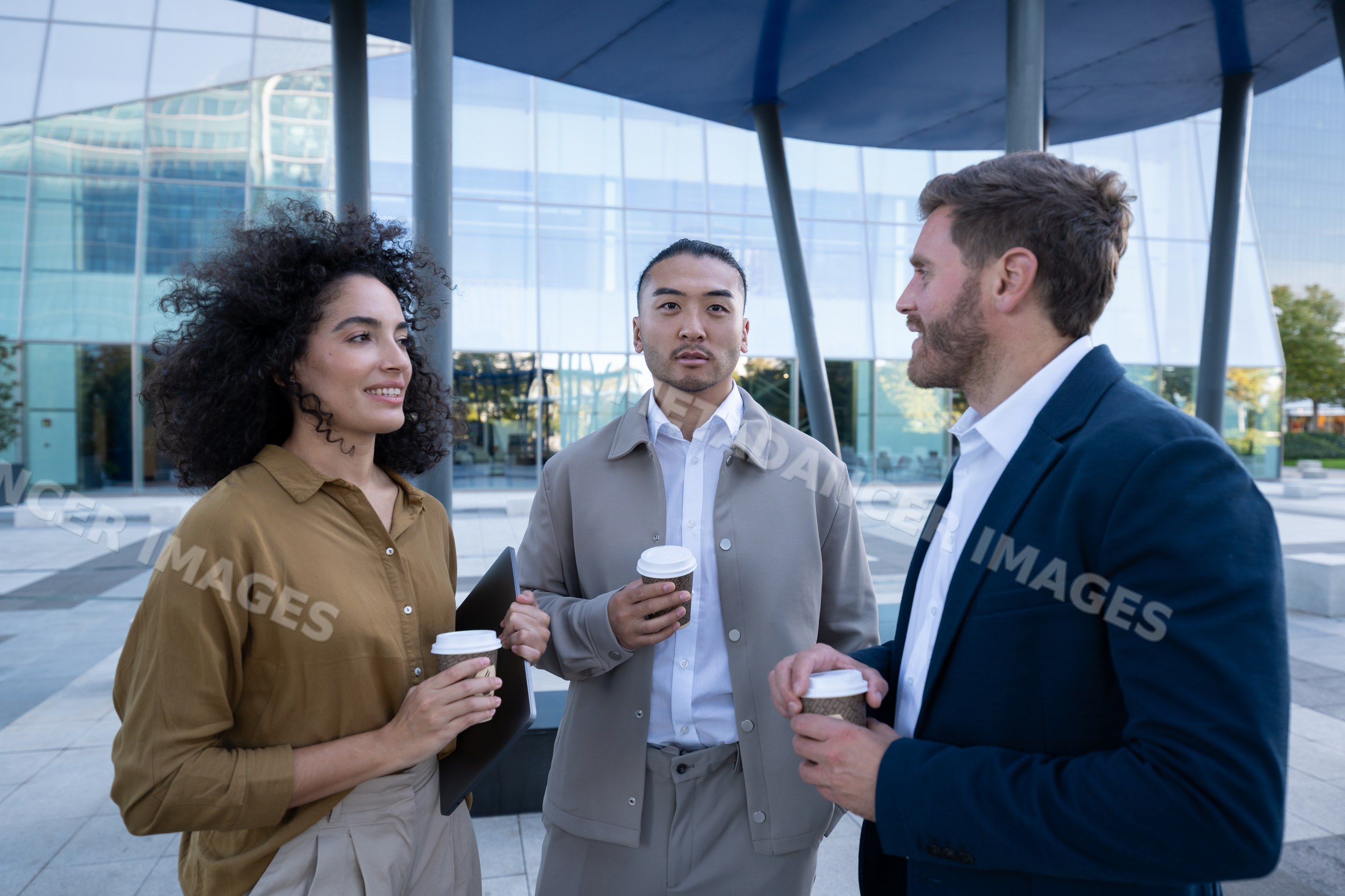 Three young white professionals holding coffee cups conversing outside