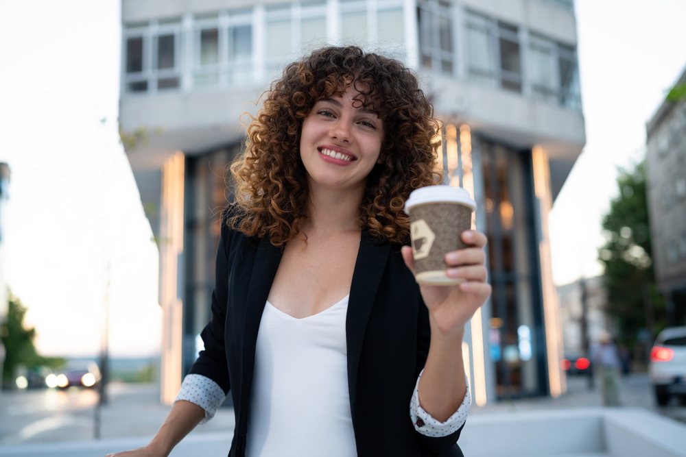 Young white woman holding coffee cup on urban street in a street
