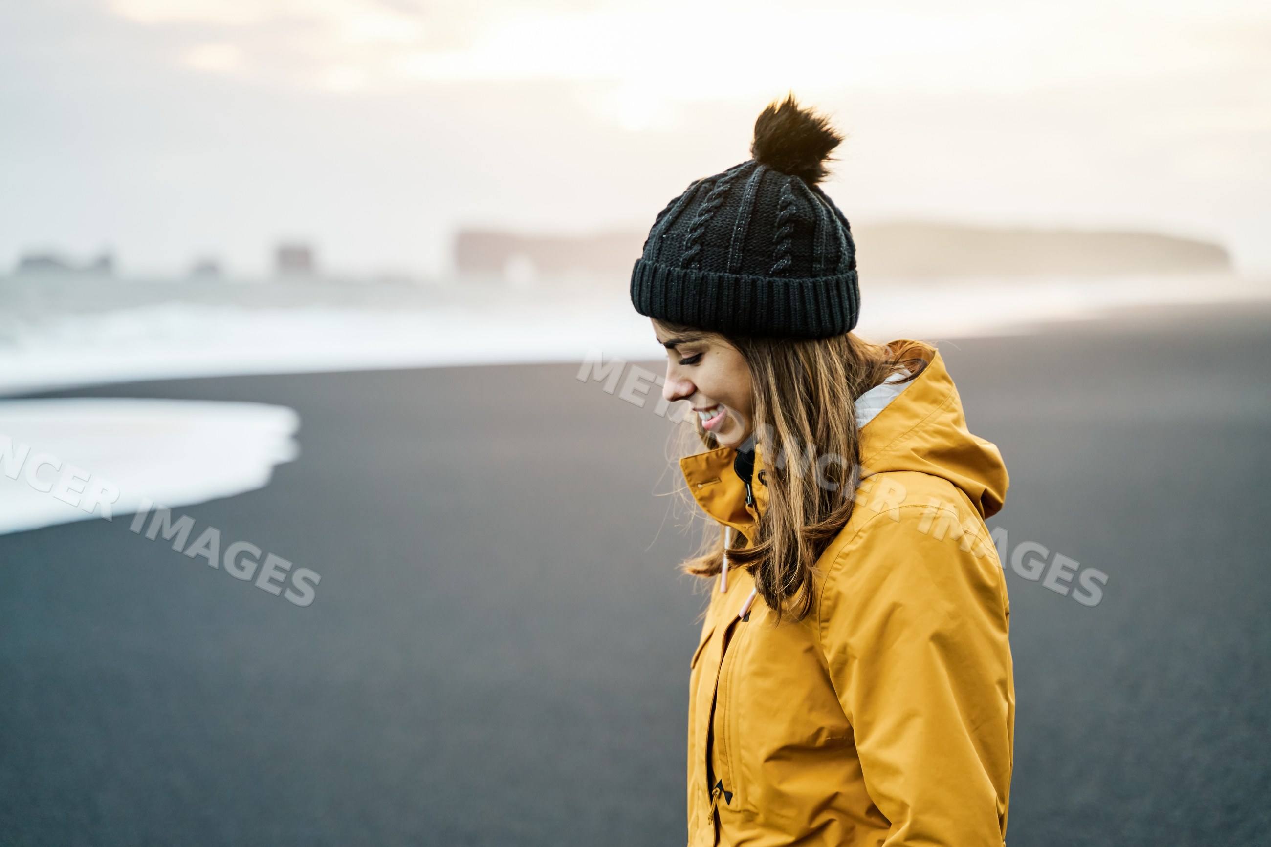 A white woman in a yellow jacket enjoys standing on a black sand beach