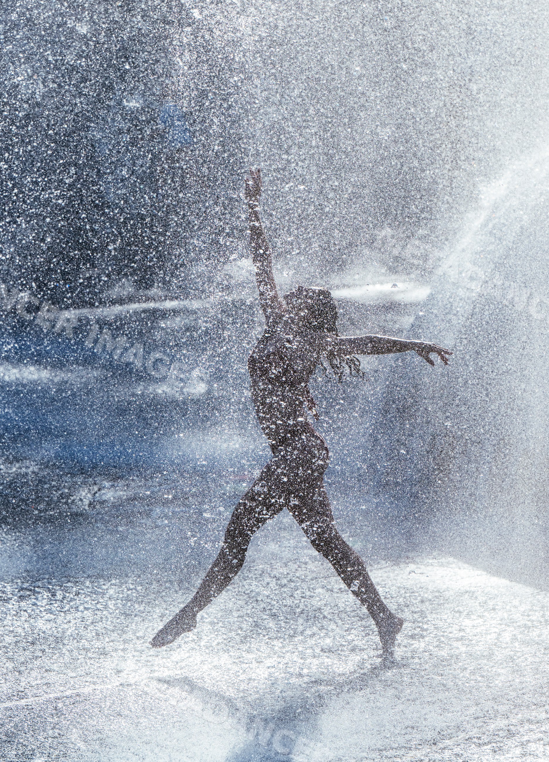 White female dancer jumping gracefully through water spray outdoors