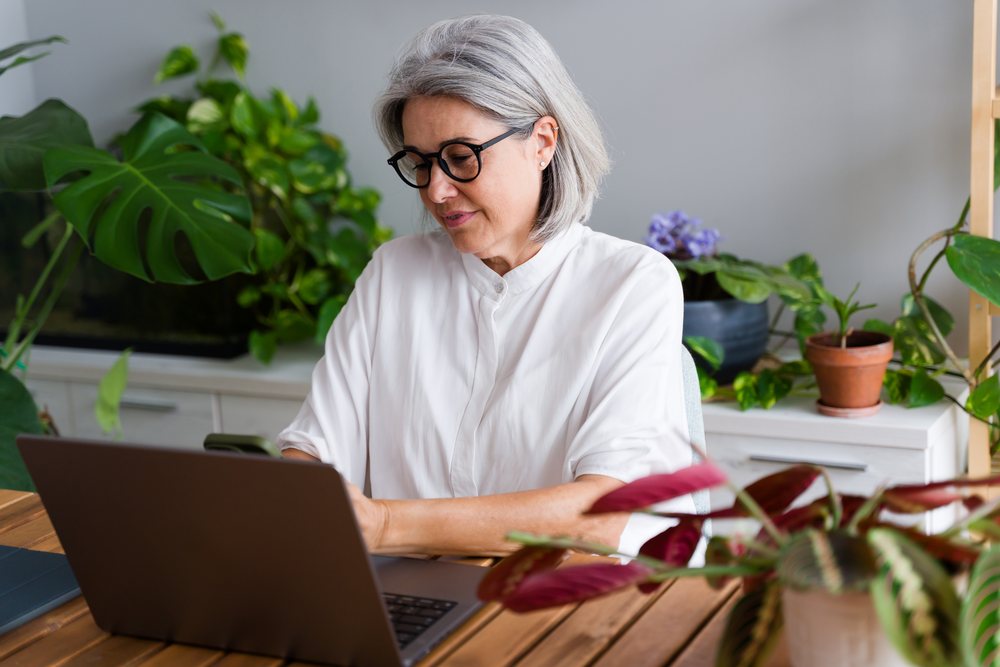 White Woman with gray hair working on laptop with smartphone