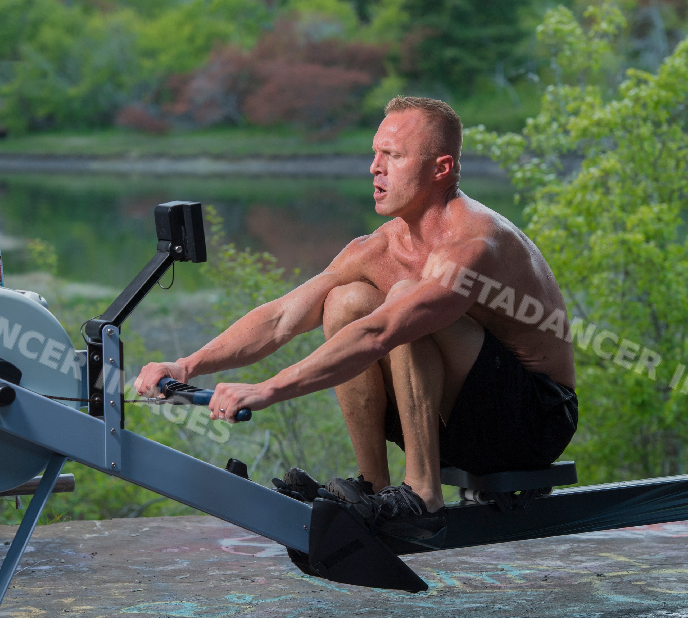 White man exercising on rowing machine outdoors near lake