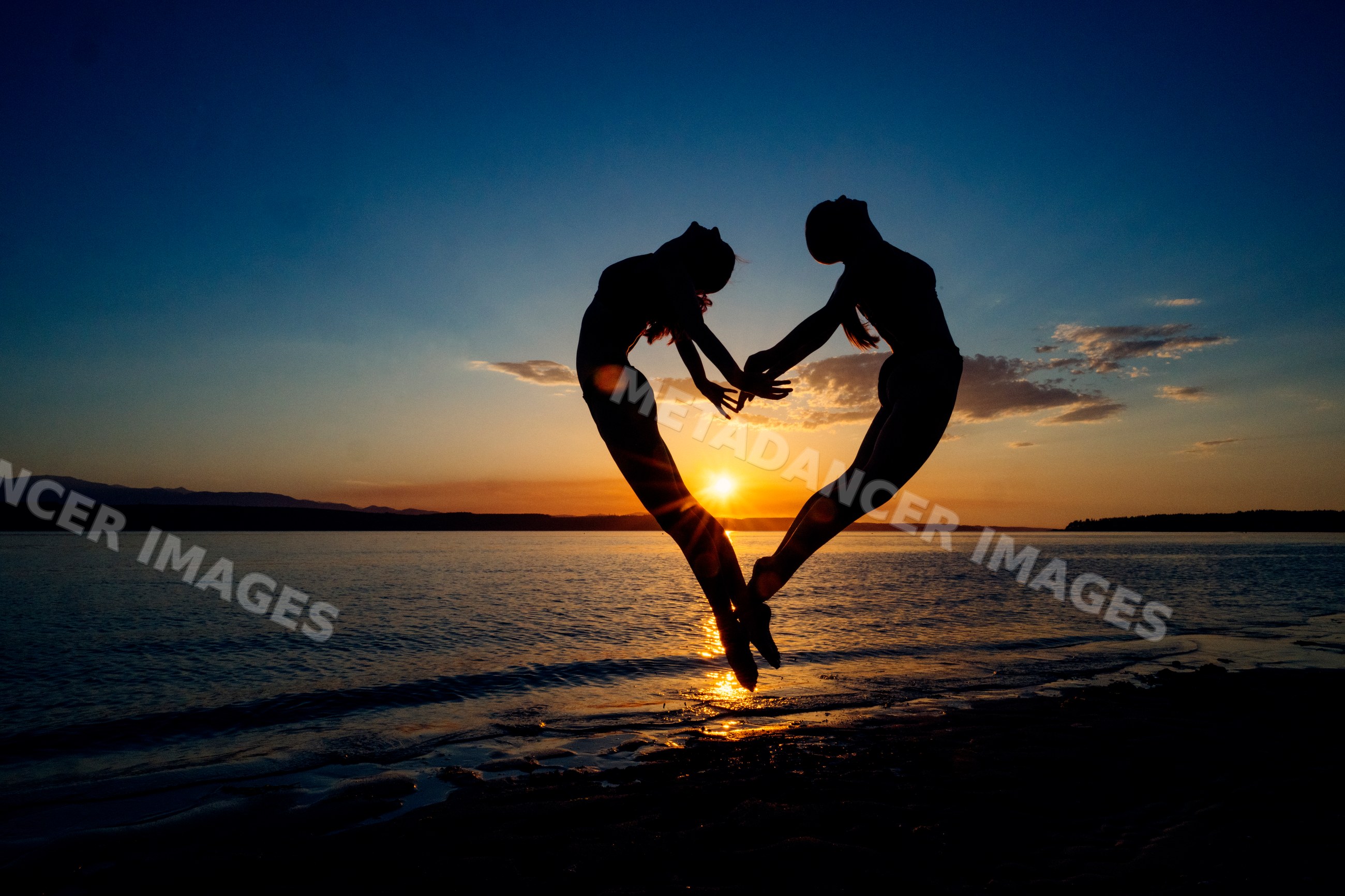 Two white people perform partner yoga acrobatics together