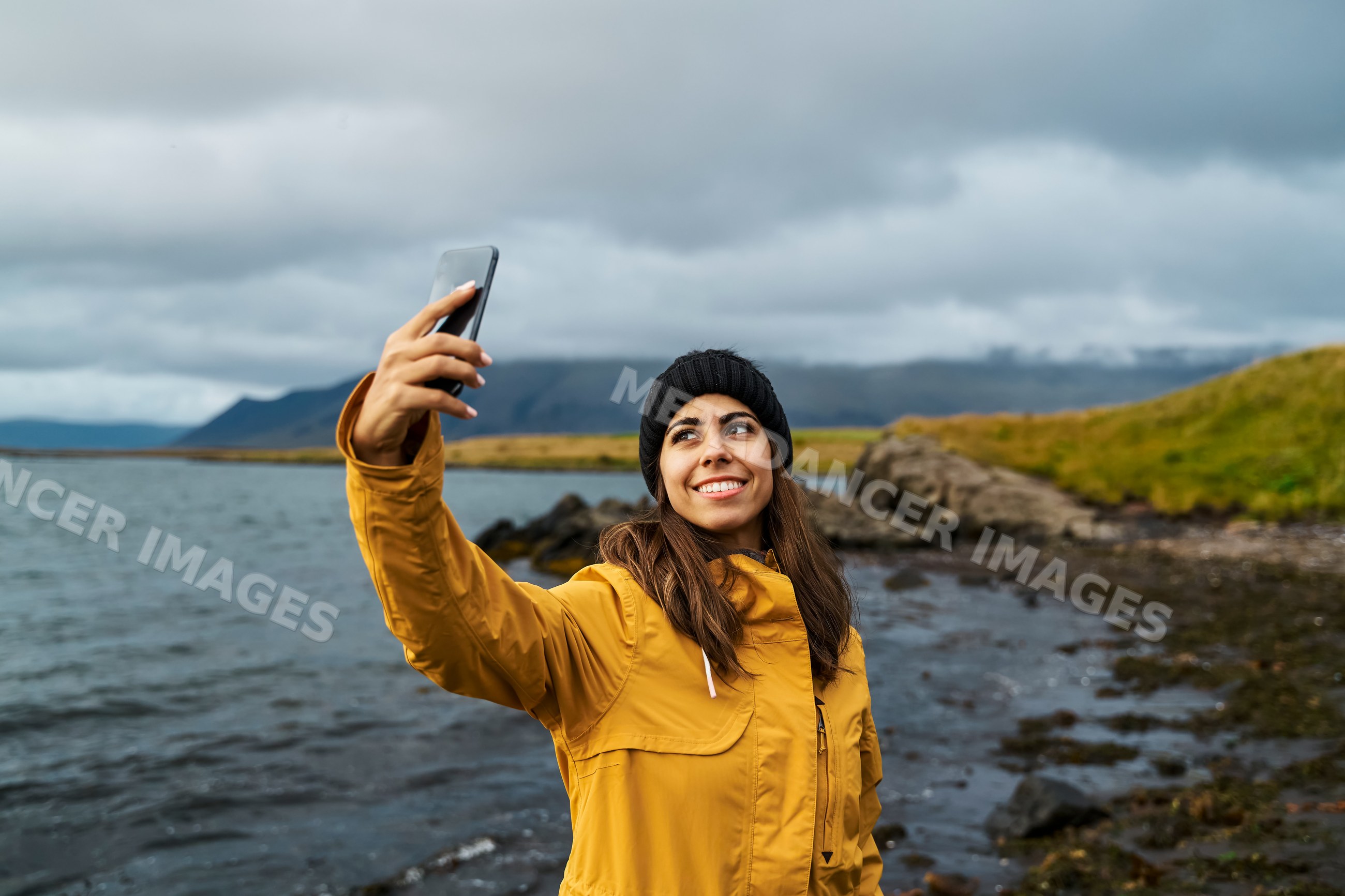 Young white woman takes selfie at rocky shoreline in Iceland