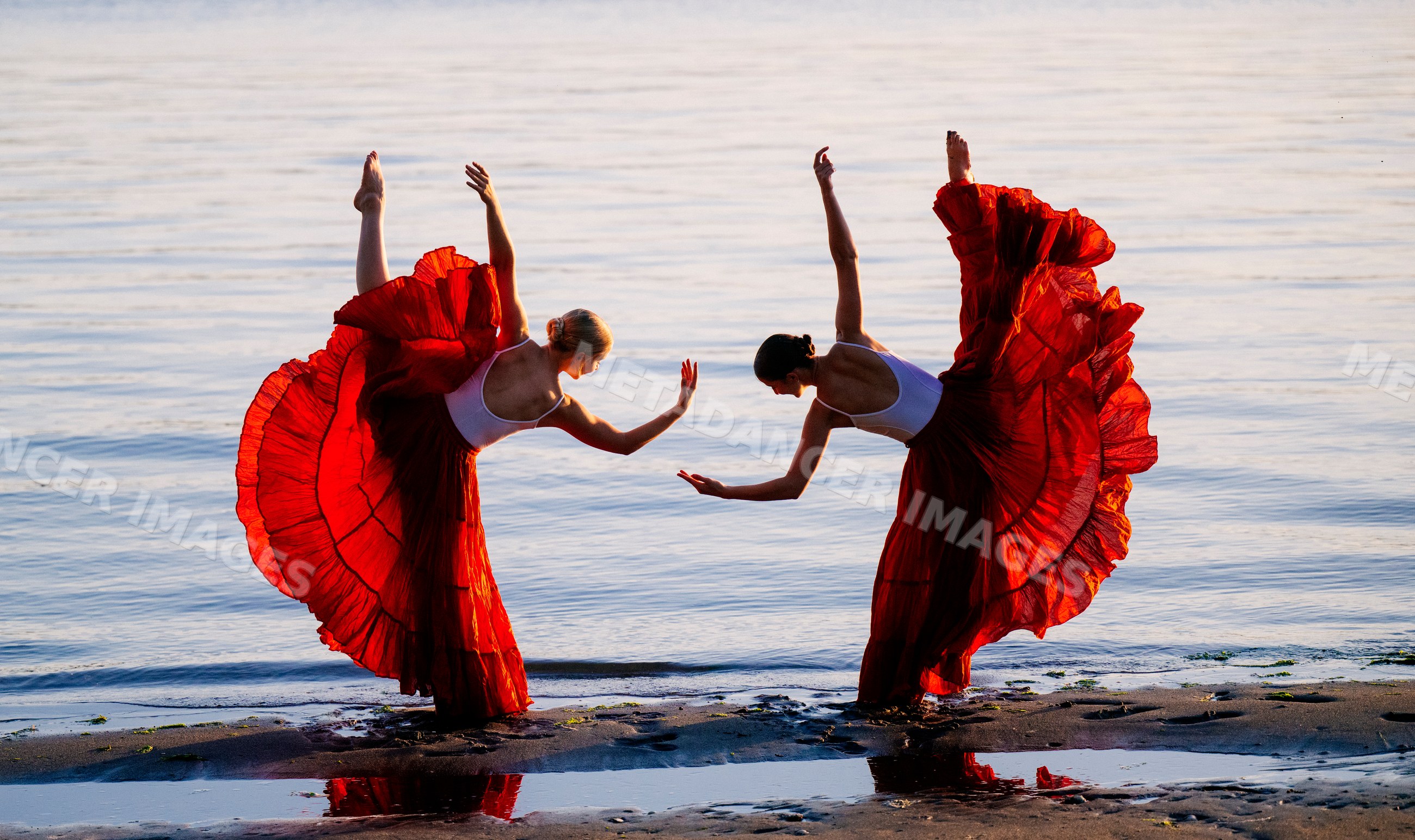 Two white women performing partner acrobatics yoga on a beach