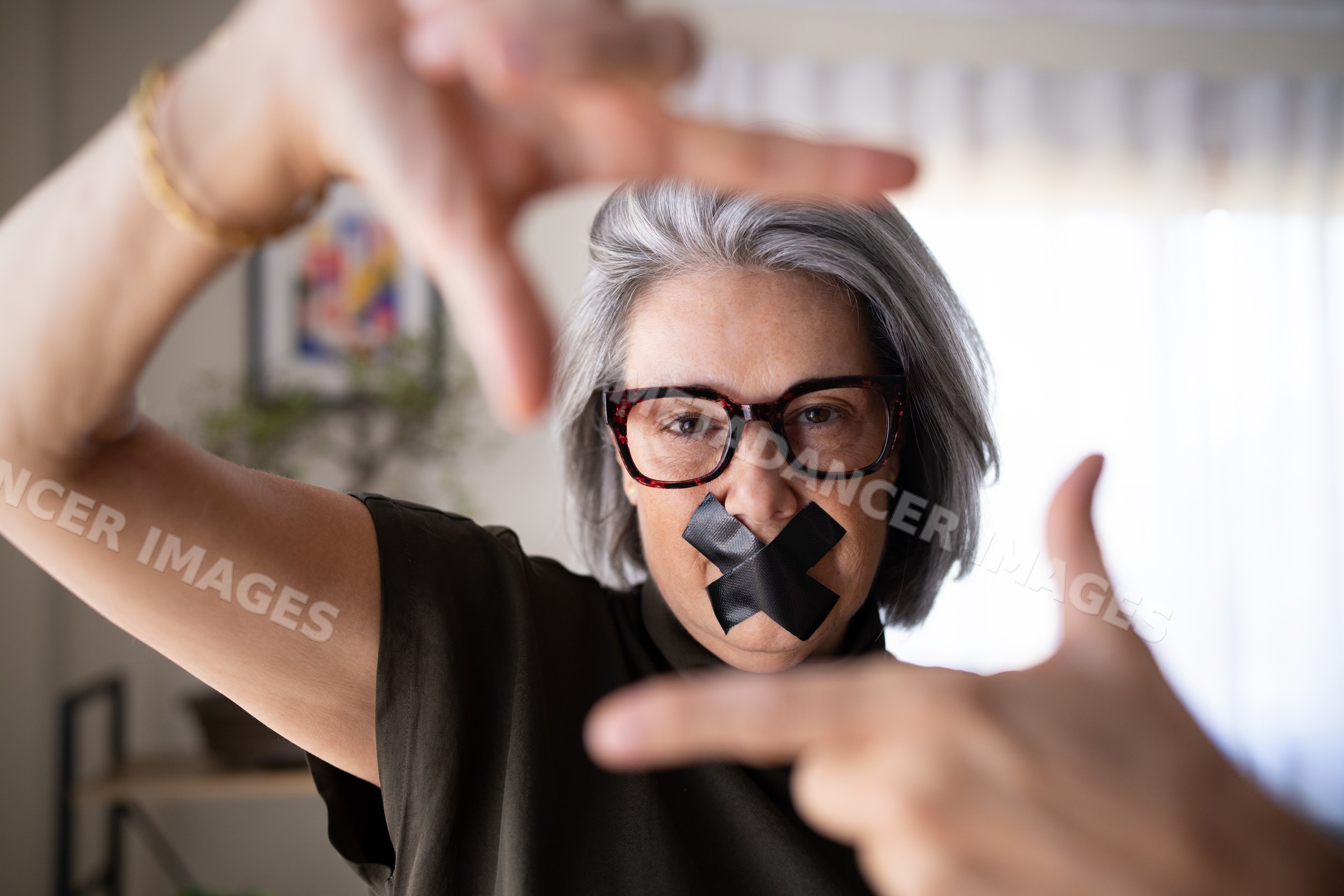White woman framing face with hands and black tape over mouth indoors