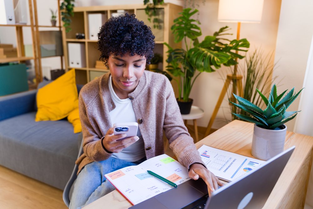 African American woman working remotely with smartphone and laptop