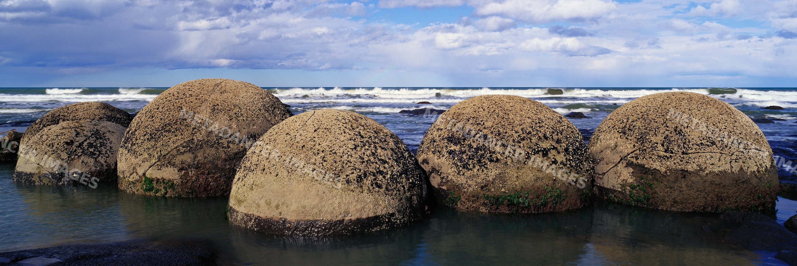 Moeraki boulders on beach with ocean waves under cloudy sky