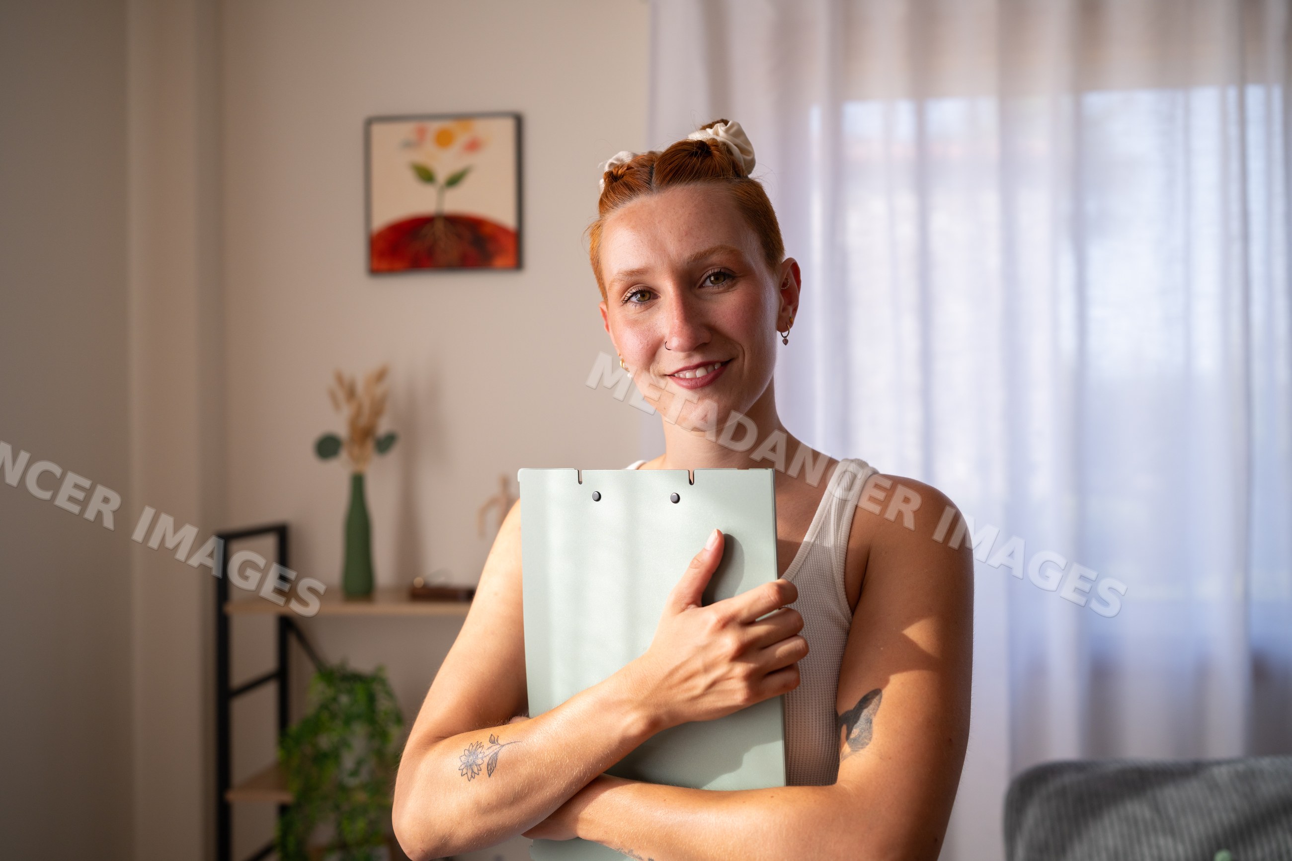 A smiling white woman holds a folder in a bright home office setting