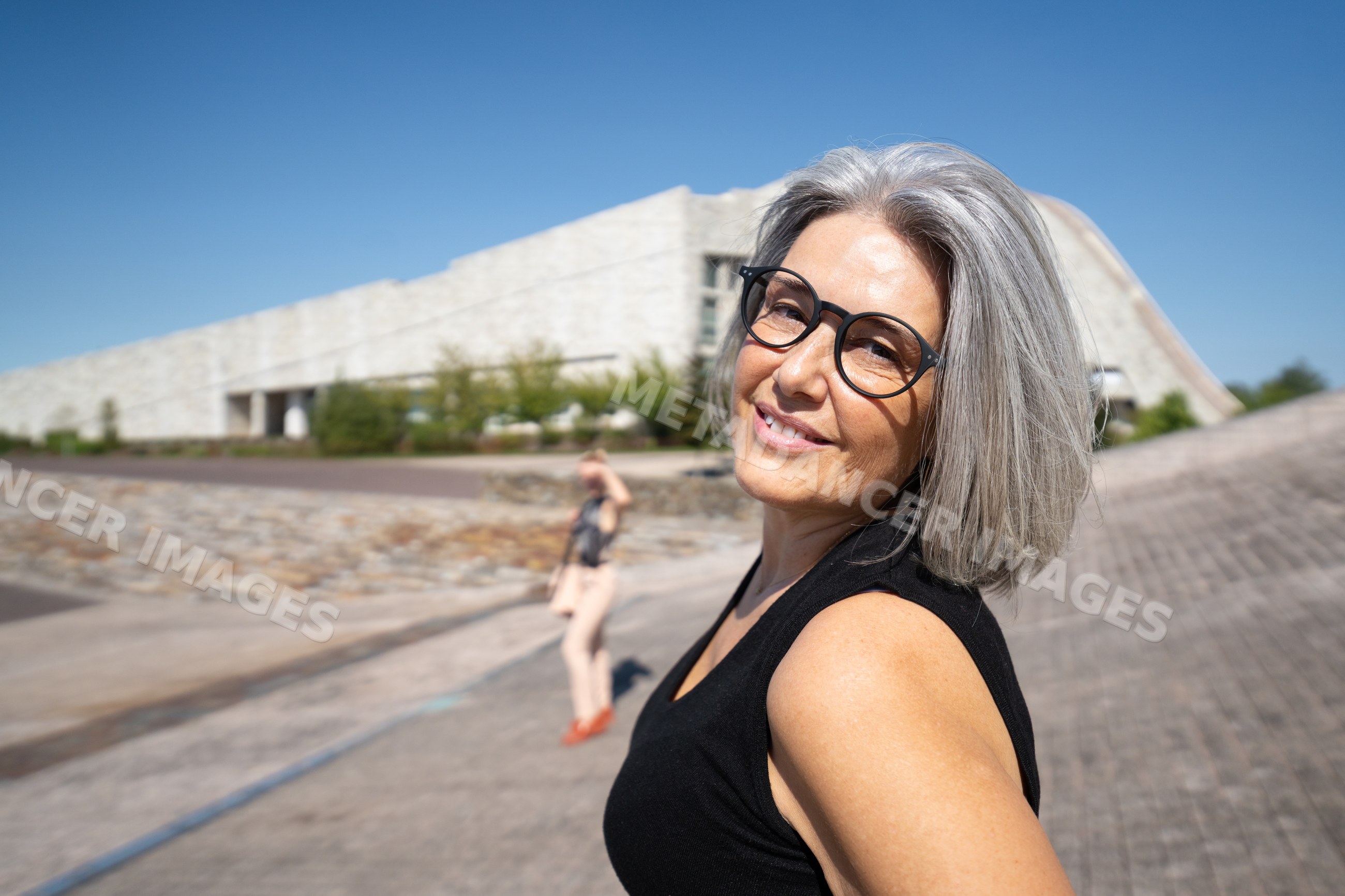White woman with gray hair smiling outdoors near a modern building