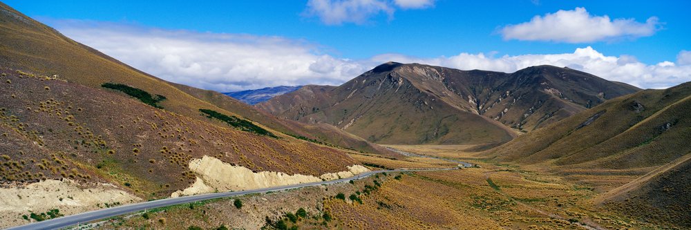 Road winding through a mountain pass with scenic hills and blue sky