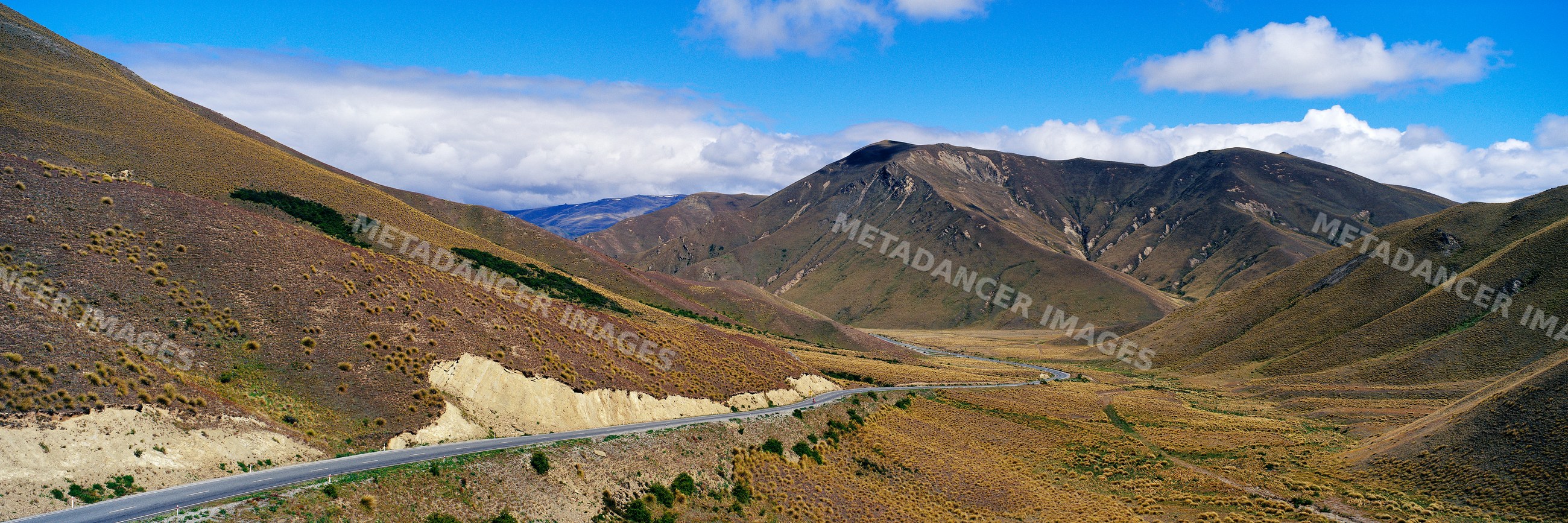 Road winding through a mountain pass with scenic hills and blue sky