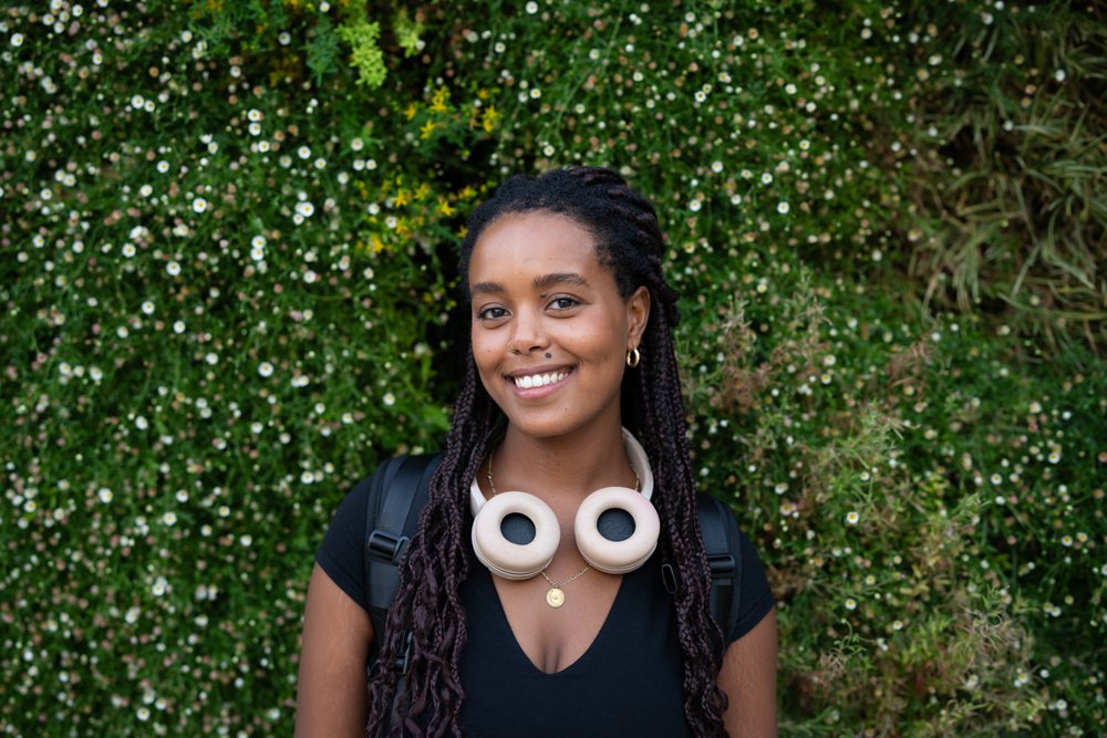 A young African American woman with headphones smiles outdoors