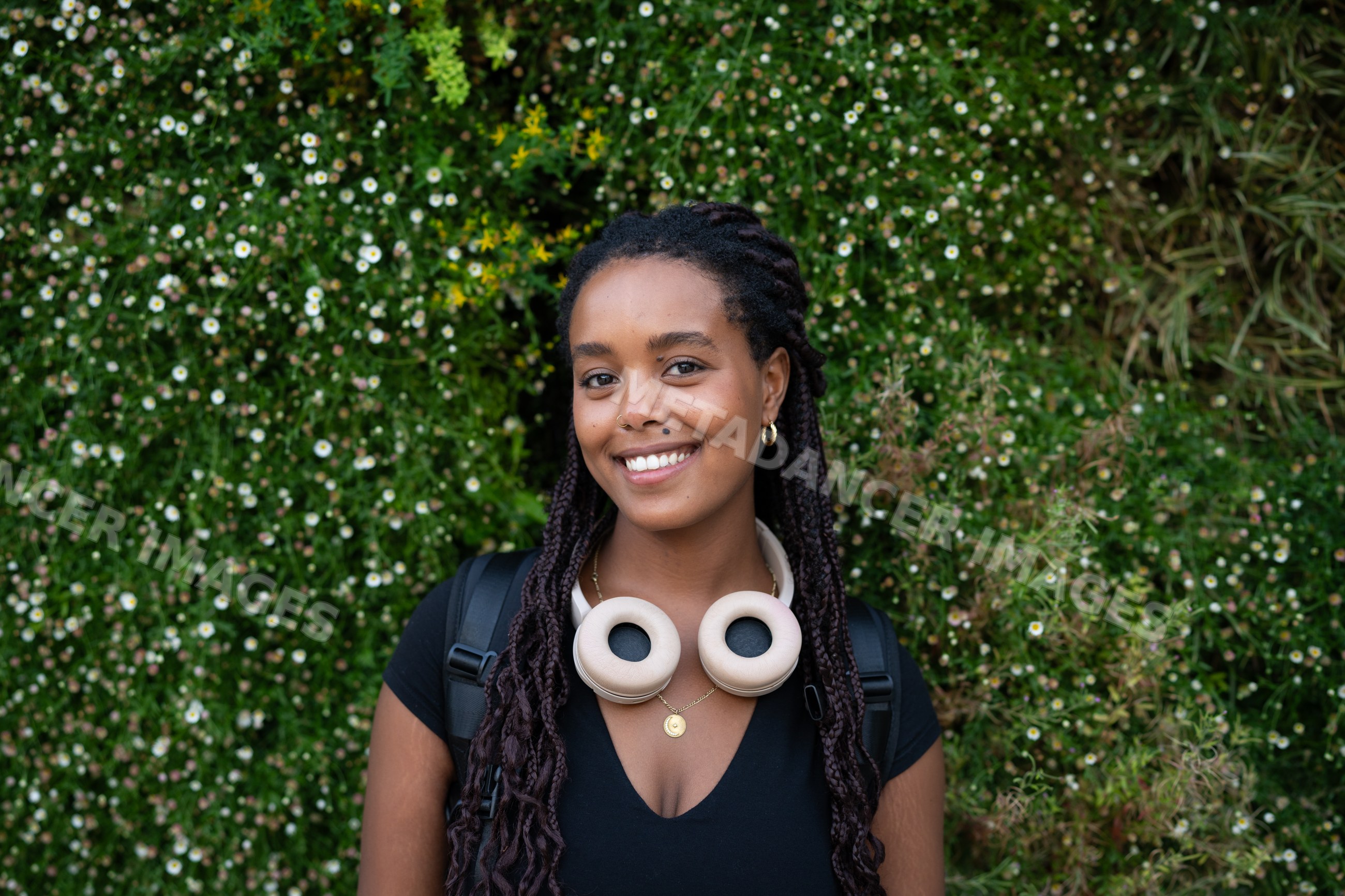 A young African American woman with headphones smiles outdoors